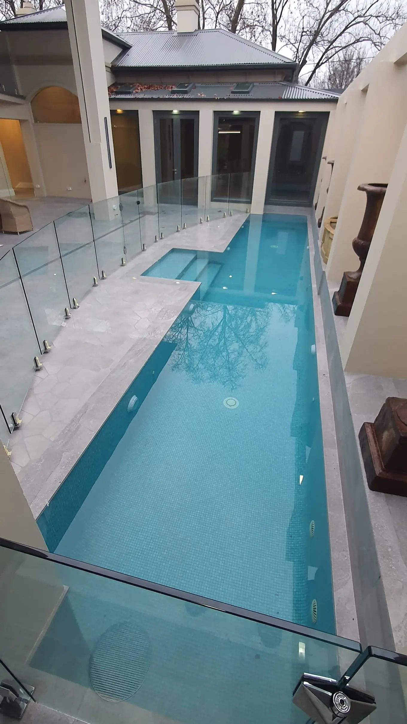 Pool with blue water and a jacuzzi, surrounded by glass fencing, stone walls, and a building — David Son Tiling in Springdale Heights, NSW