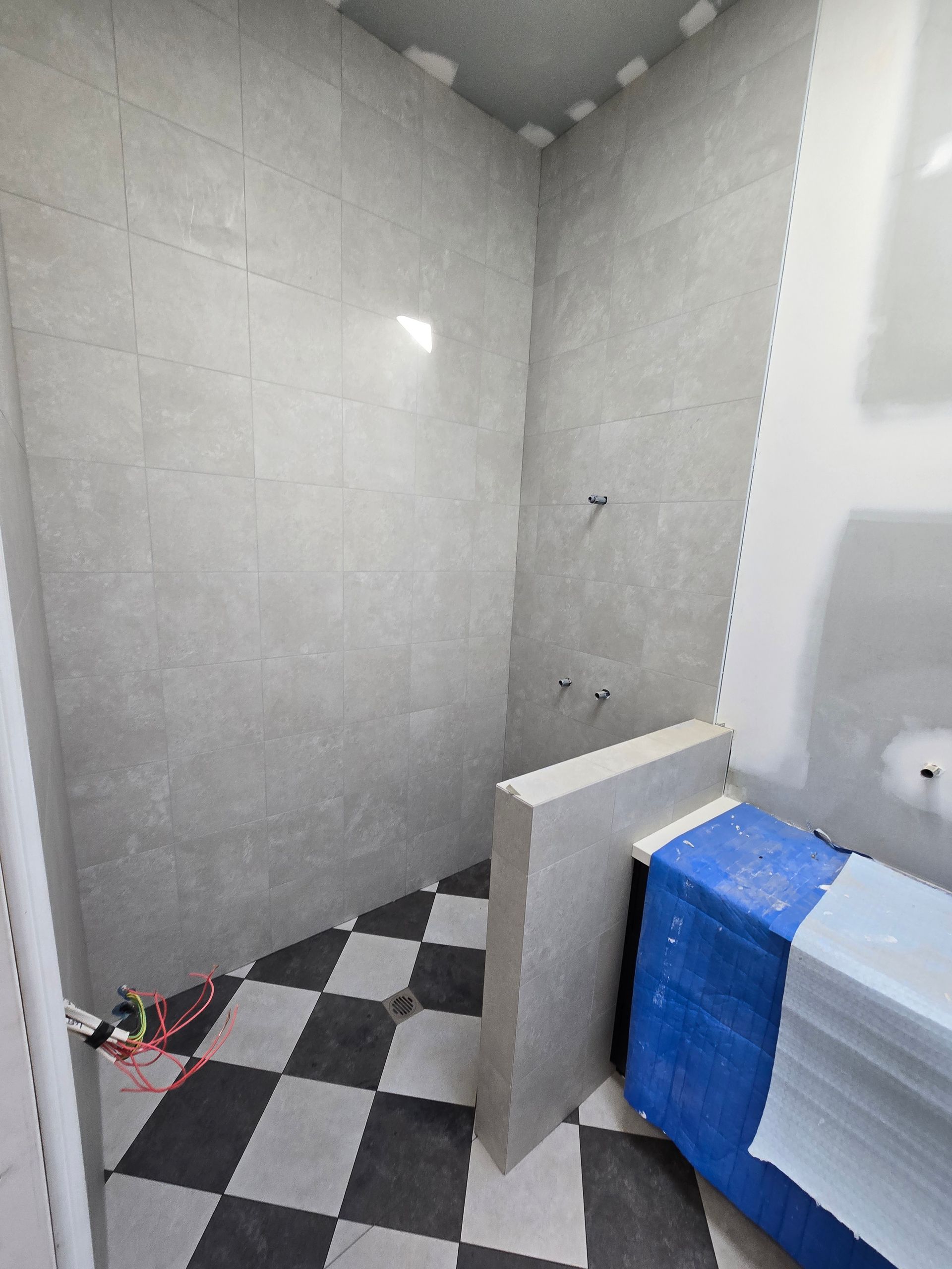 Bathroom under construction with grey tiled walls, checkered floor, and building materials — David Son Tiling in Springdale Heights, NSW