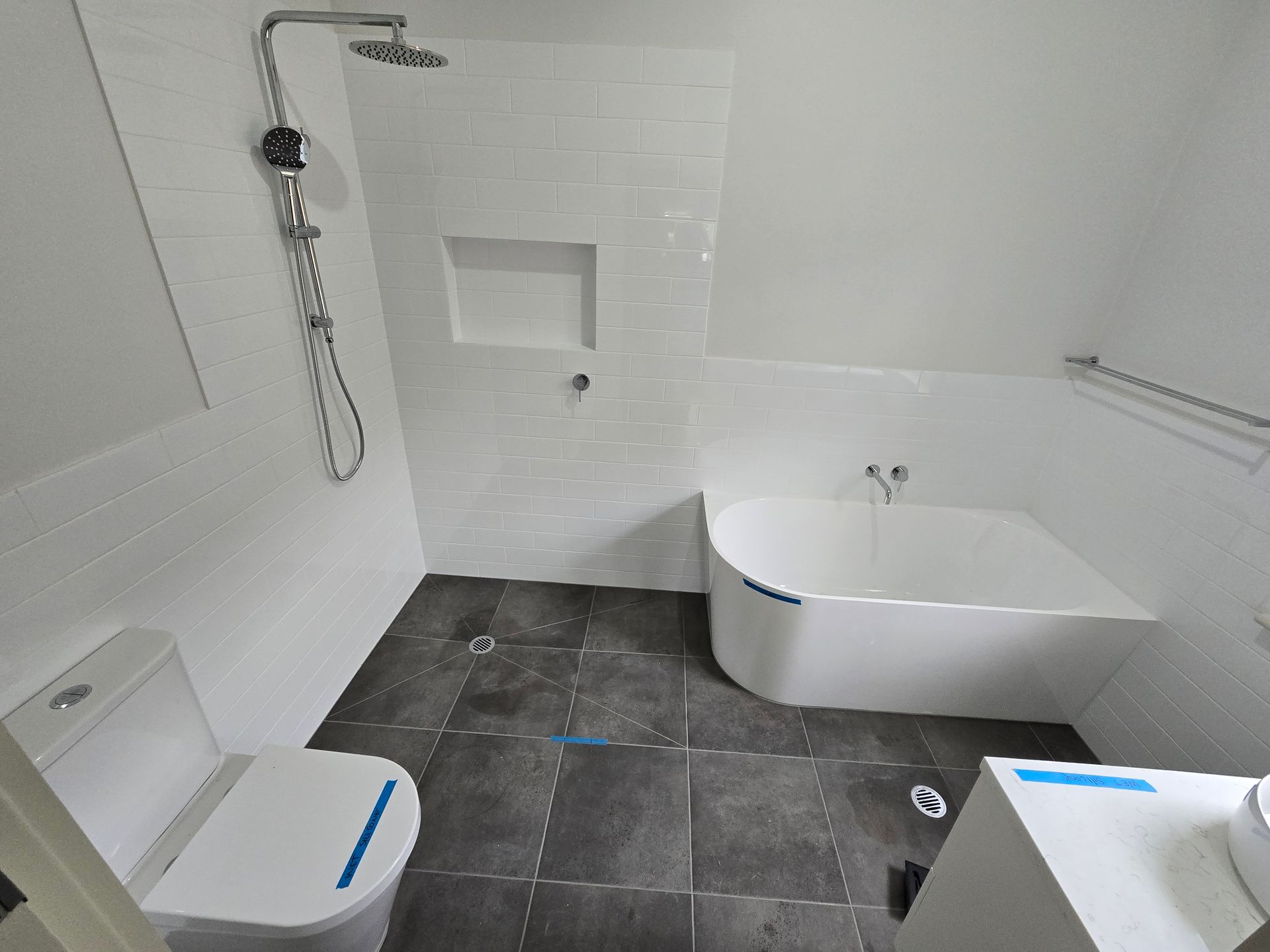 Bathroom with white tiling, shower, toilet, tub, dark grey tiled floor, and vanity — David Son Tiling in Springdale Heights, NSW