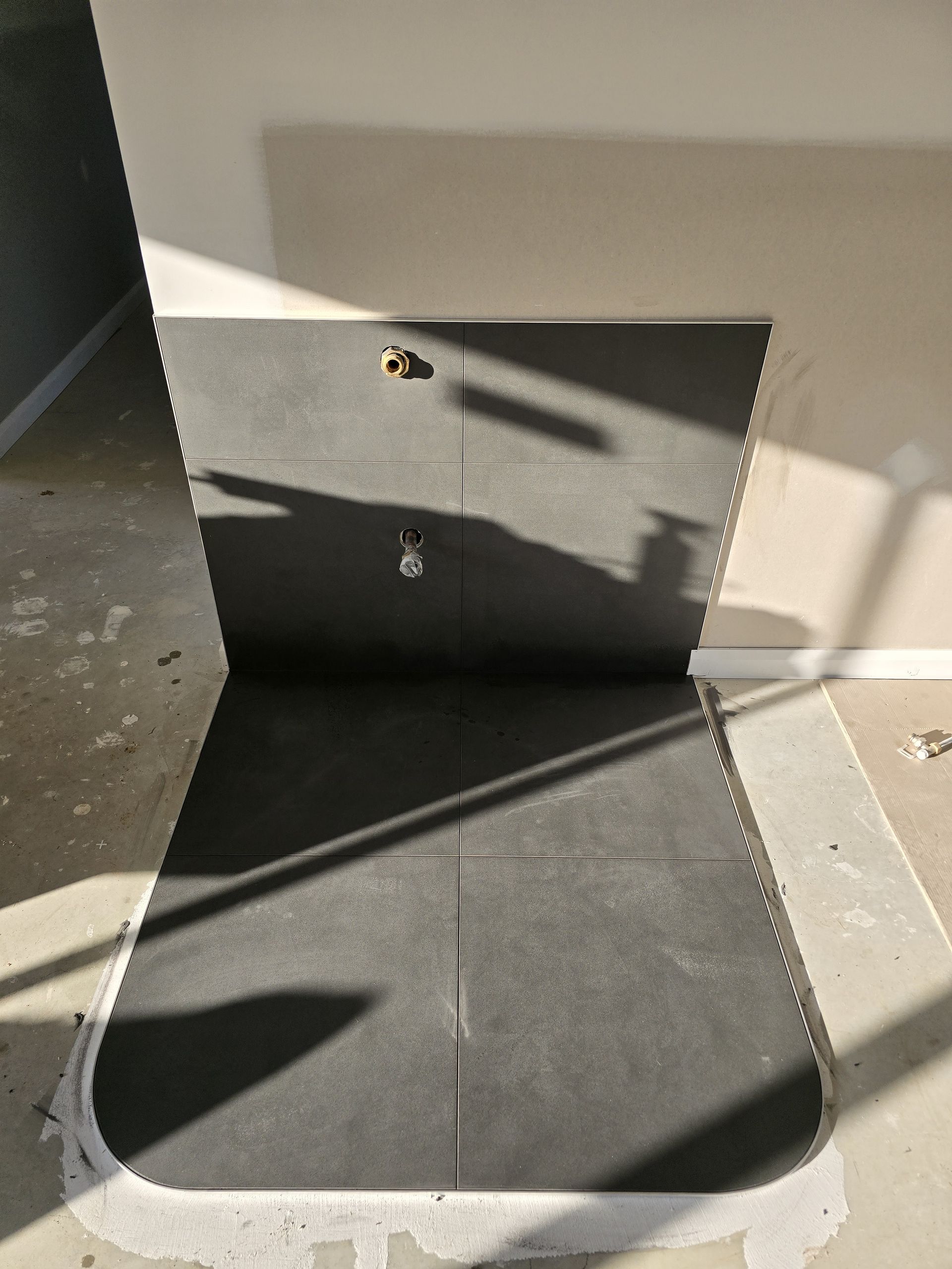 A grey tiled niche in a wall with two brass fixtures; white walls and a concrete floor — David Son Tiling in Springdale Heights, NSW