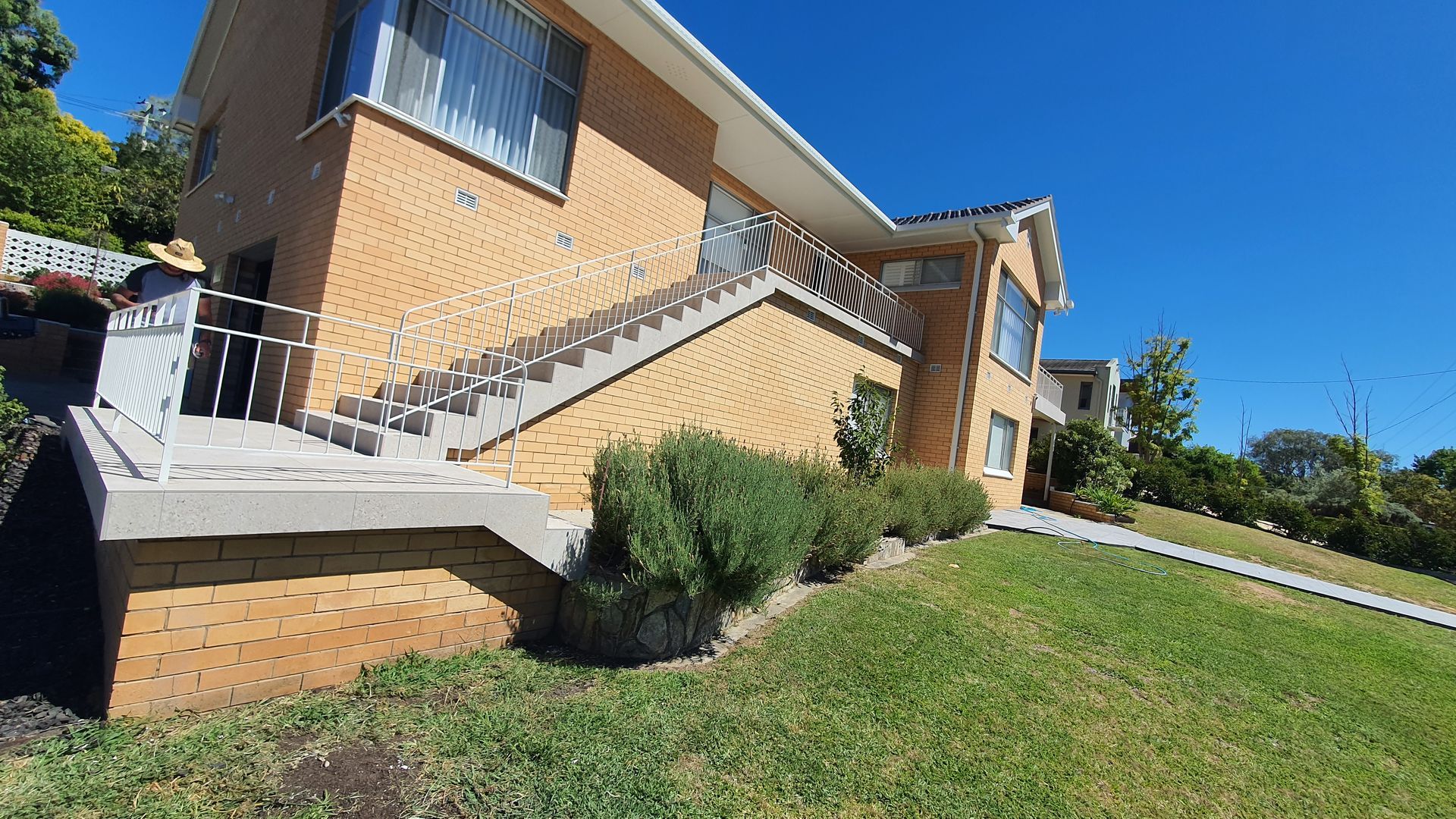 Brick apartment building with outside stairs on a grassy hill under a bright blue sky — David Son Tiling in Springdale Heights, NSW