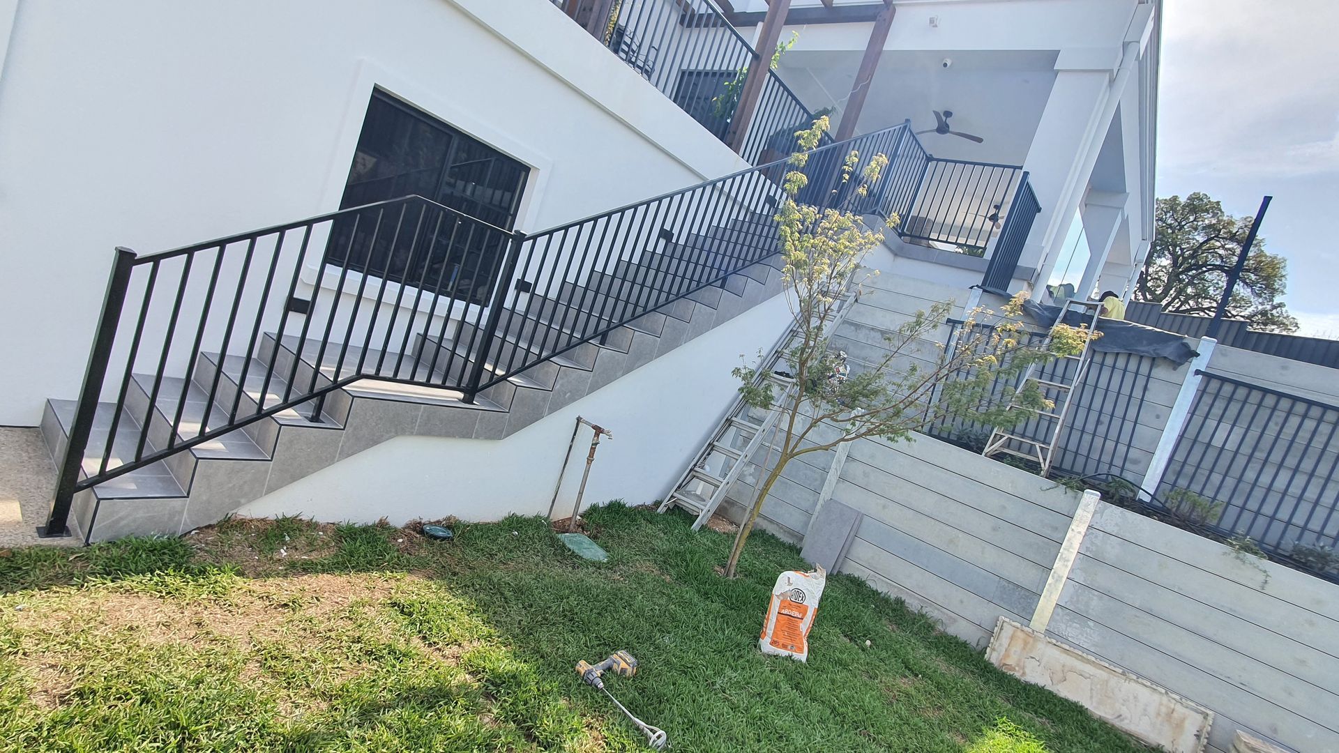 Exterior staircase with black railing leading up a white building with a grassy lawn — David Son Tiling in Springdale Heights, NSW