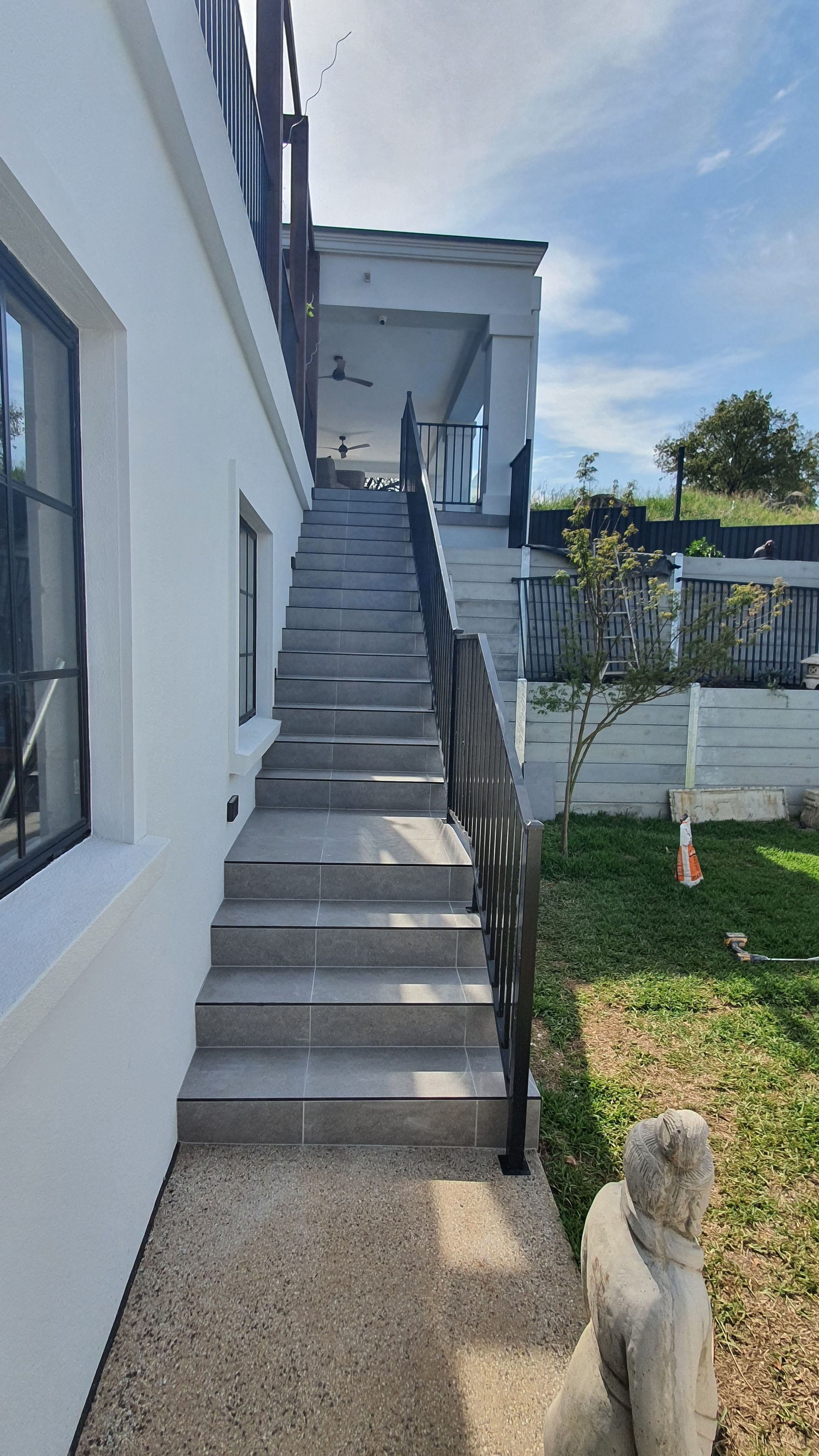 Exterior shot of grey concrete stairs leading to a white house, with black railings, and a grassy area — David Son Tiling in Springdale Heights, NSW