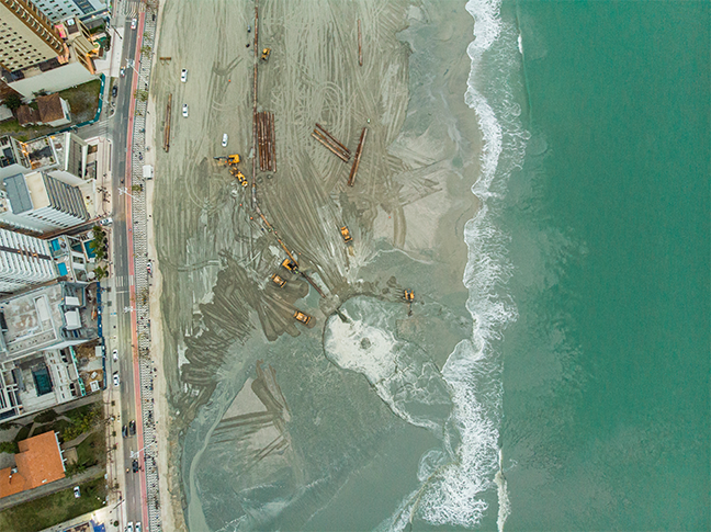 Uma vista aérea de uma praia e oceano com edifícios ao fundo.
