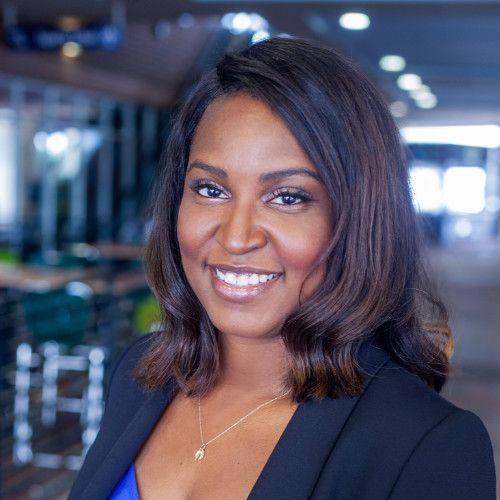 a woman in a black jacket and blue top is smiling for the camera .