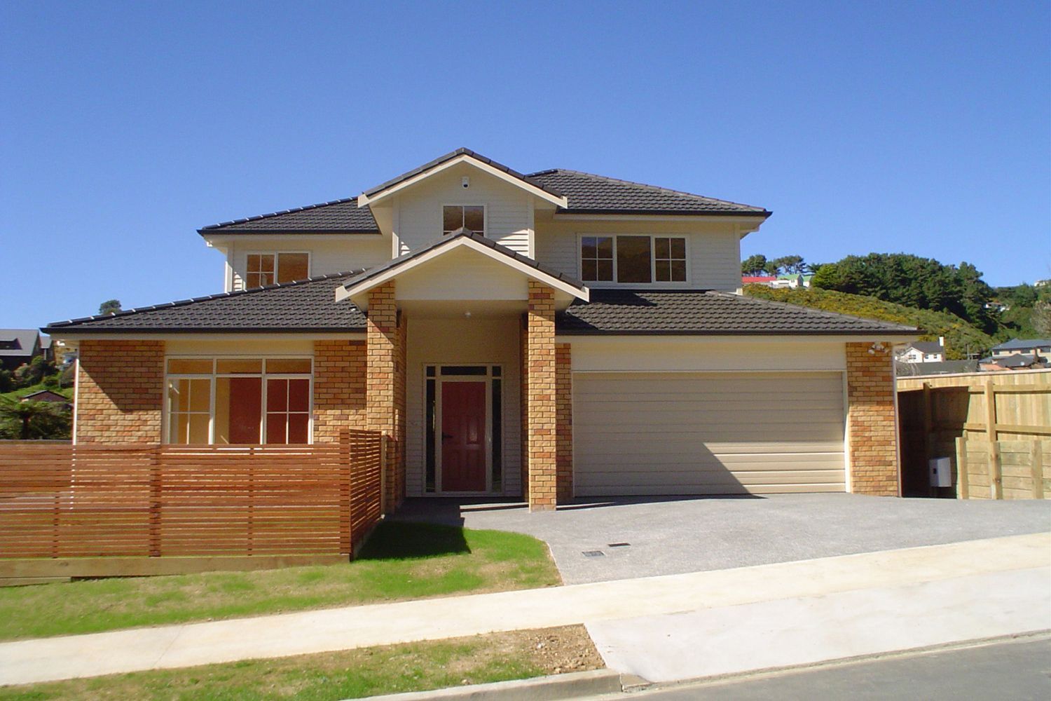 Two-story house with brick accents, gray roof, red front door, and attached garage on a sunny day.