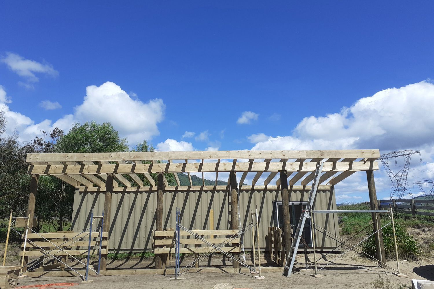 Wooden structure under construction against a blue sky, with support beams and a partial roof.