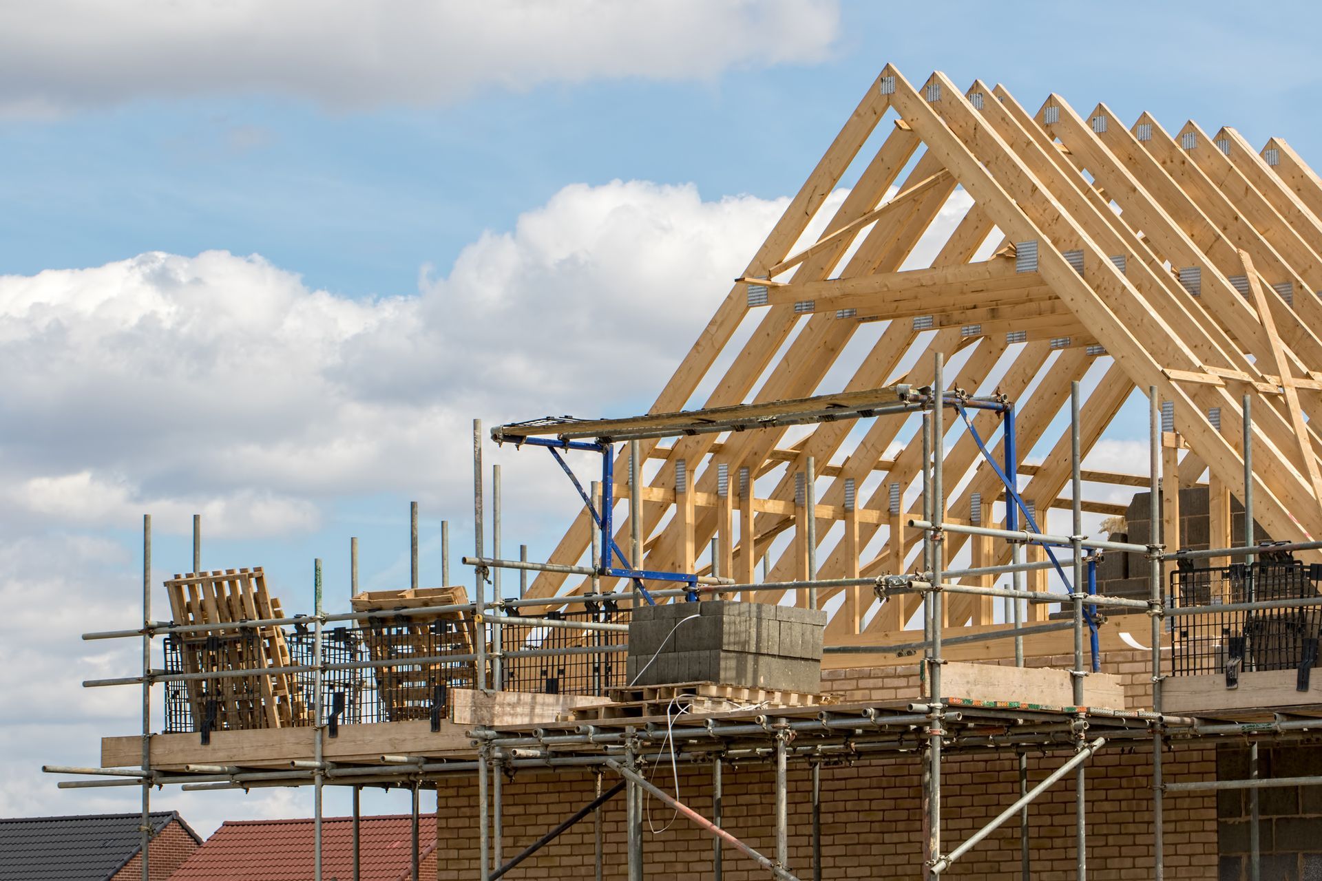 Construction site with wood roof framework and scaffolding against a cloudy sky.
