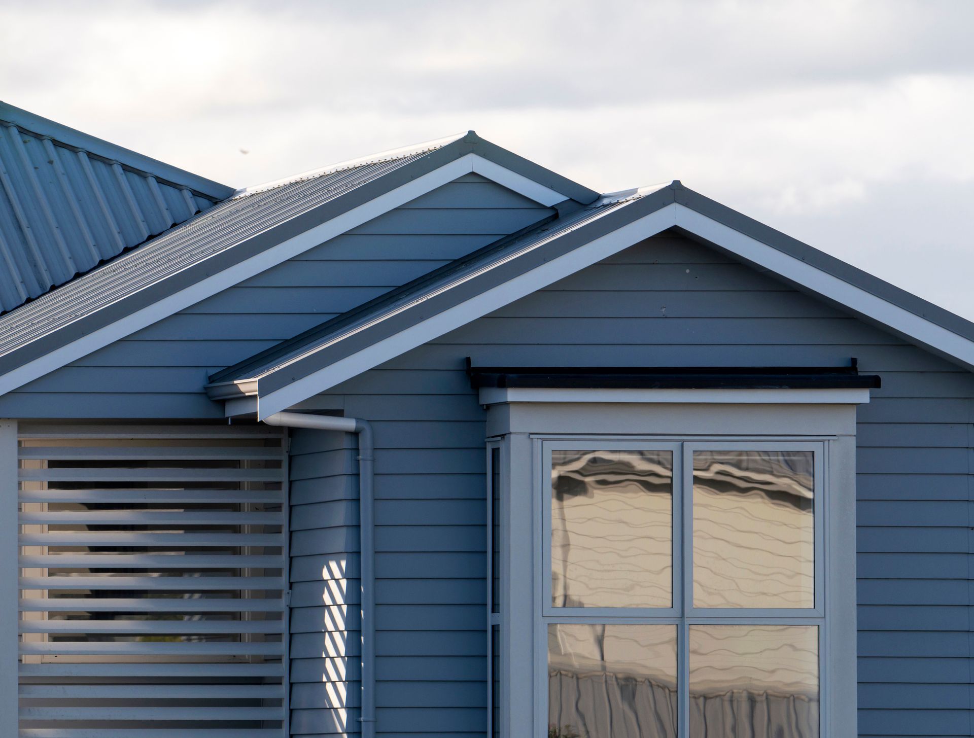 Blue house with gray metal roof, bay window reflecting light, and shuttered window.