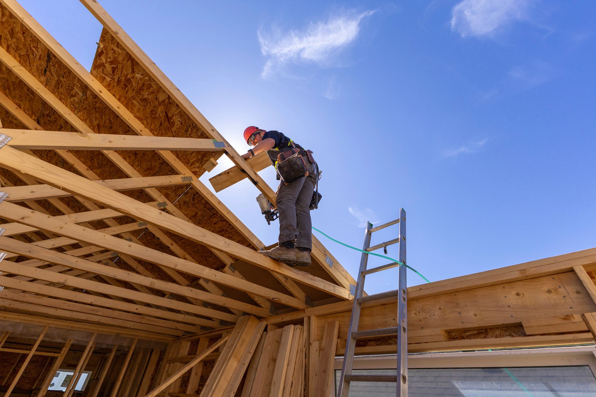 Carpenter working on roof frame under blue sky.