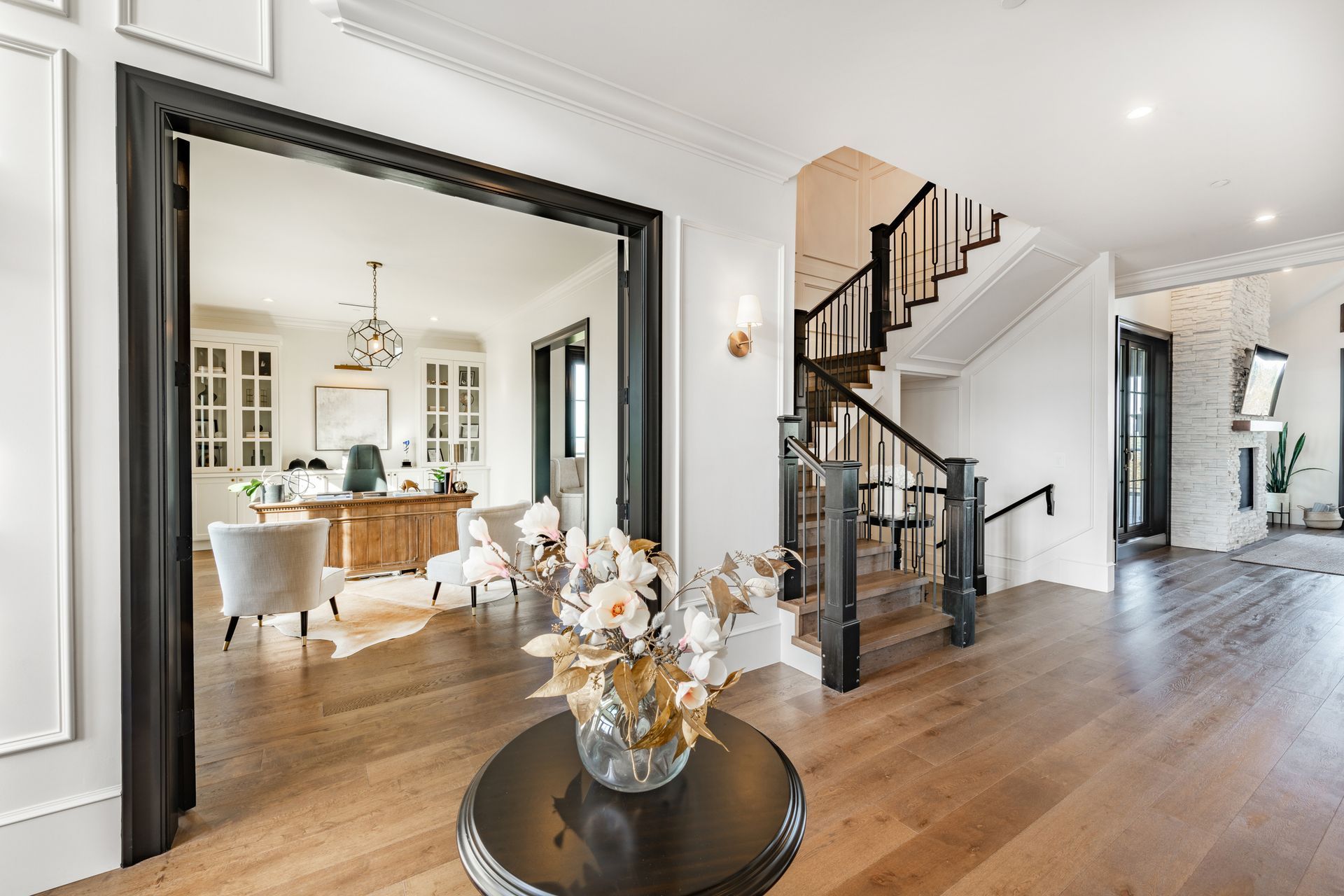 Entryway with wooden floors, black staircase, and view into a furnished room.