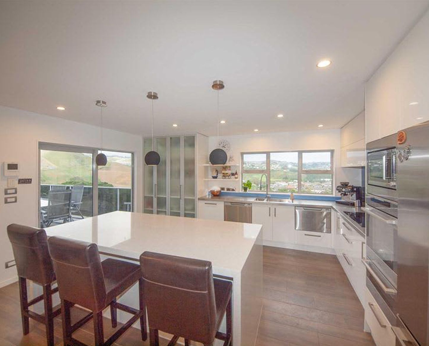 Modern kitchen with white cabinets, island, stools, and view through windows.