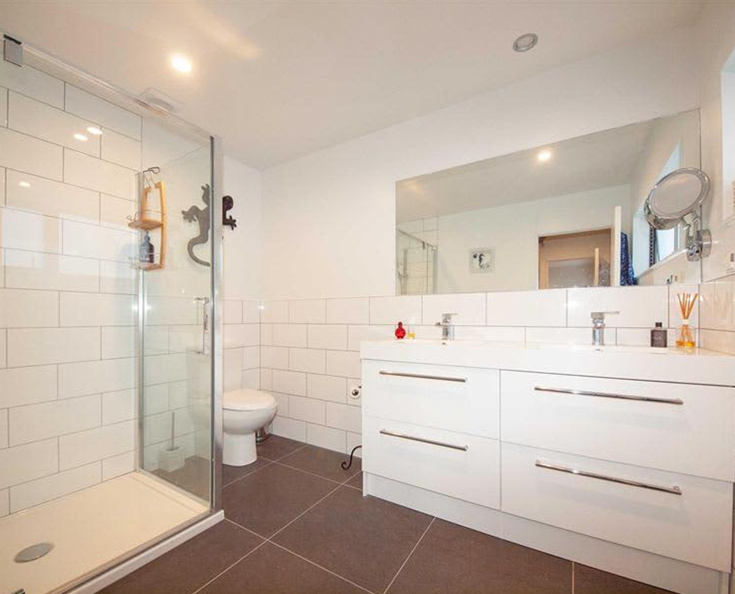 Modern bathroom with white cabinetry, glass shower, toilet, and a large mirror.