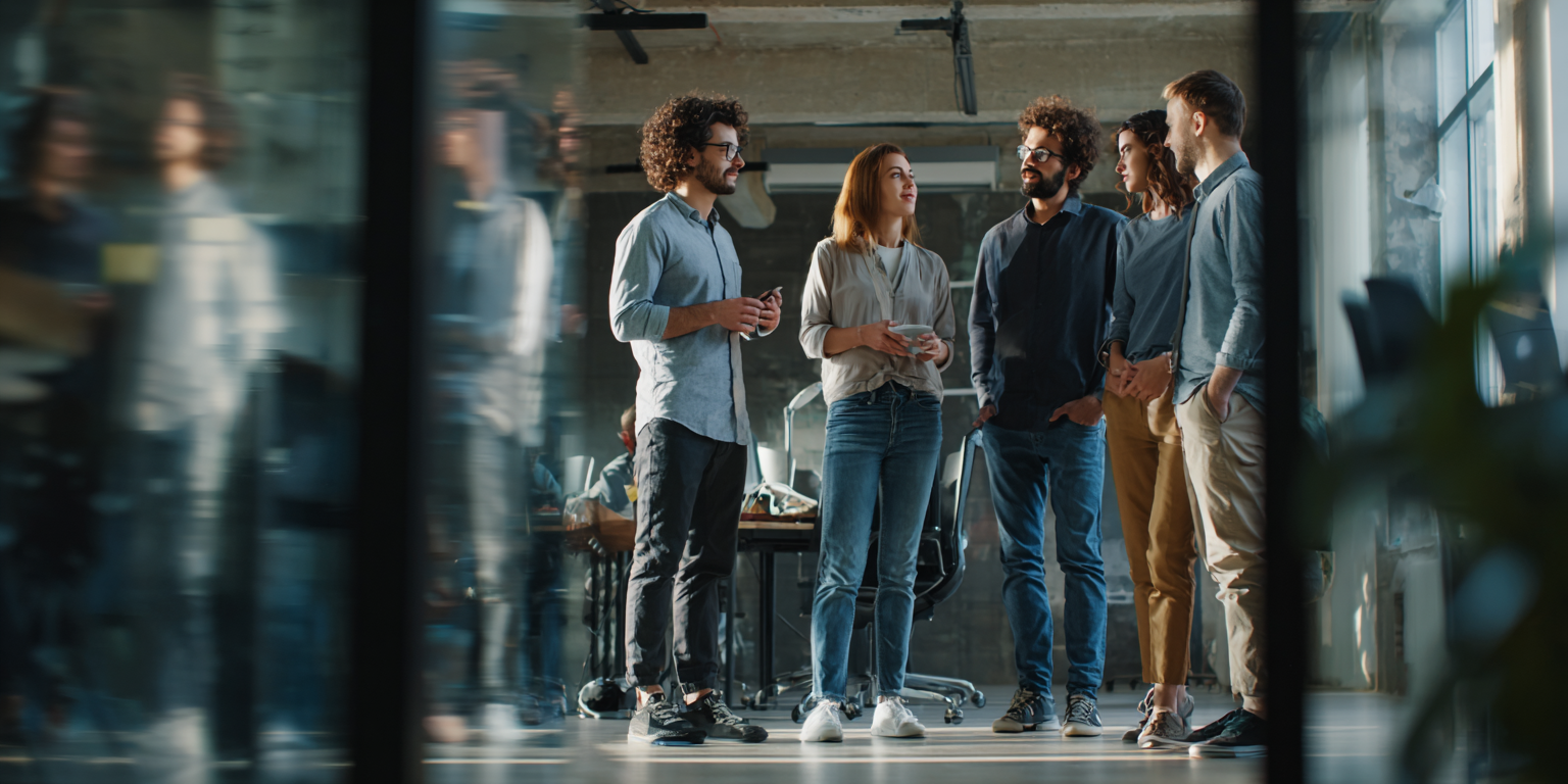 Four colleagues stand in a modern, open-plan office, engaged in a collaborative conversation.