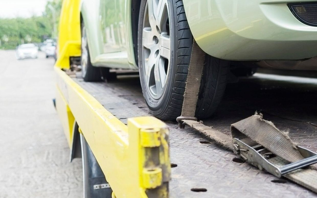 A car is being towed by a tow truck on the side of the road.