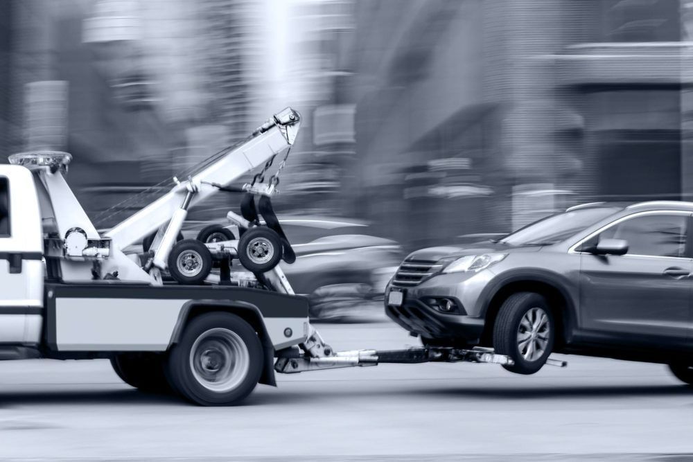 A tow truck is towing a car on a city street.