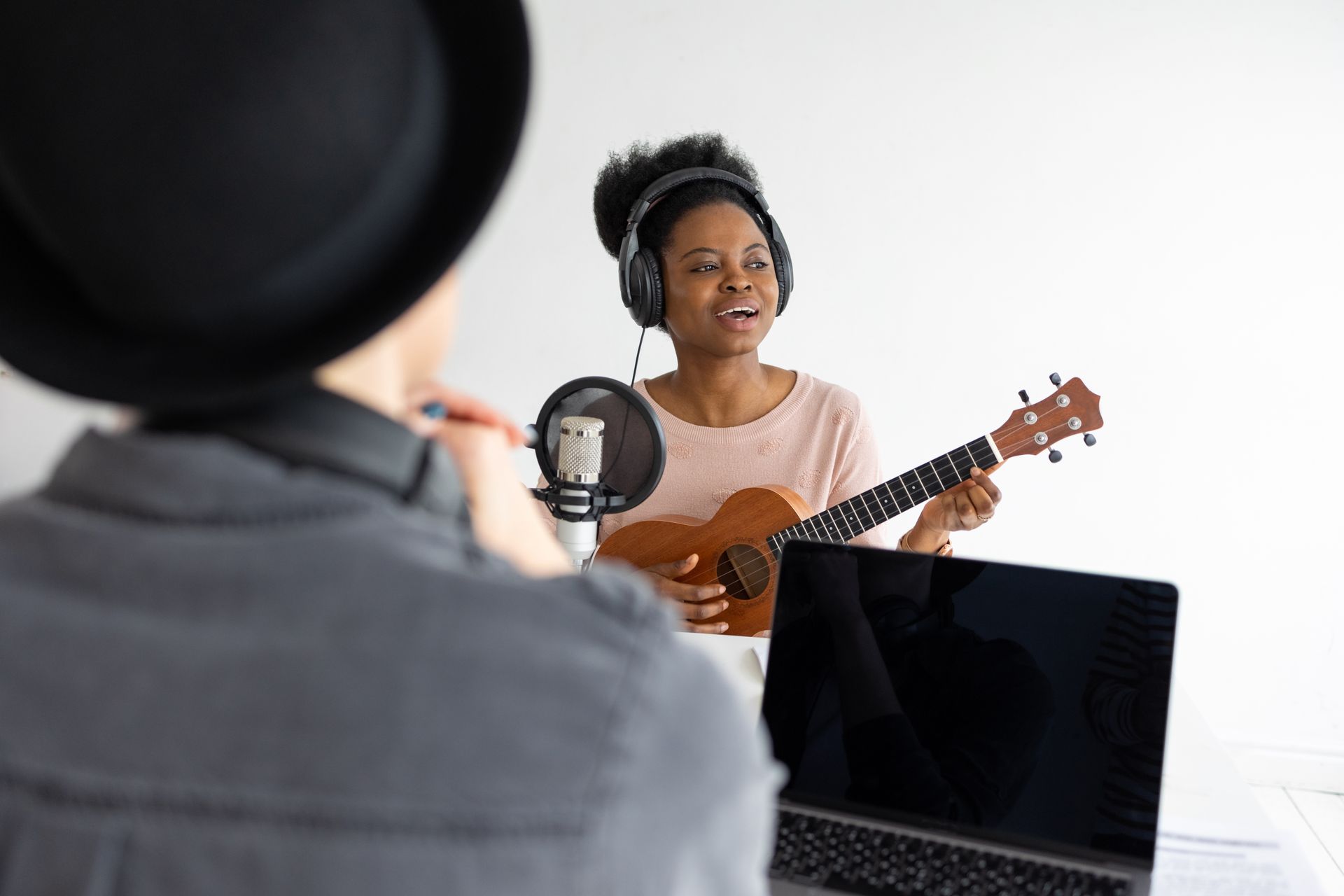 A woman is singing into a microphone while playing an ukulele.