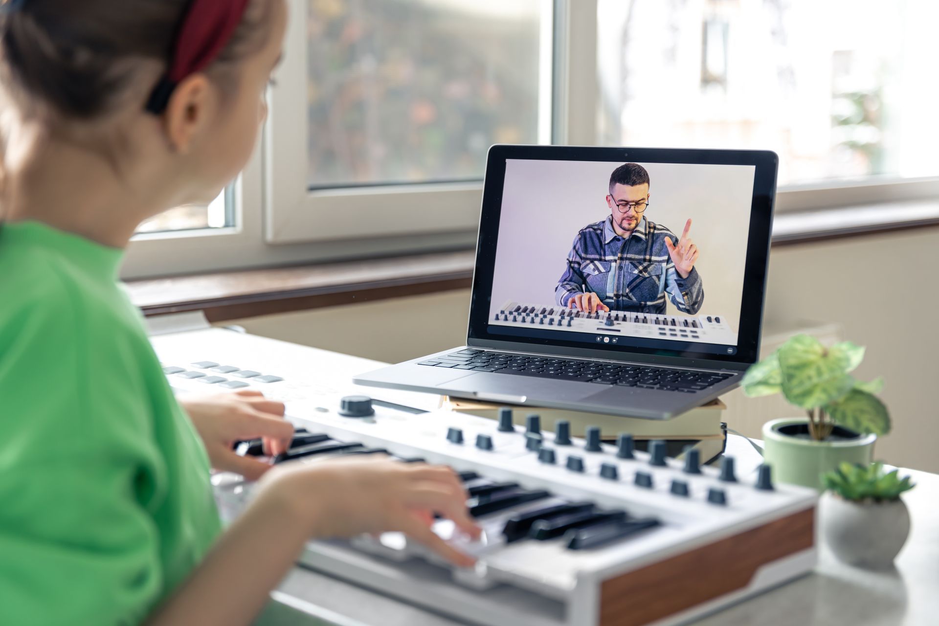 A young girl is playing a keyboard in front of a laptop computer.