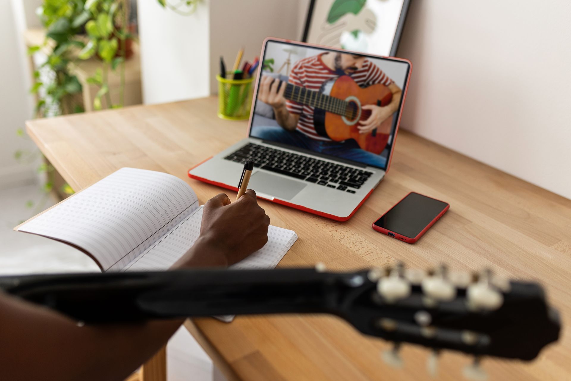 A person is sitting at a desk with a laptop and a guitar.