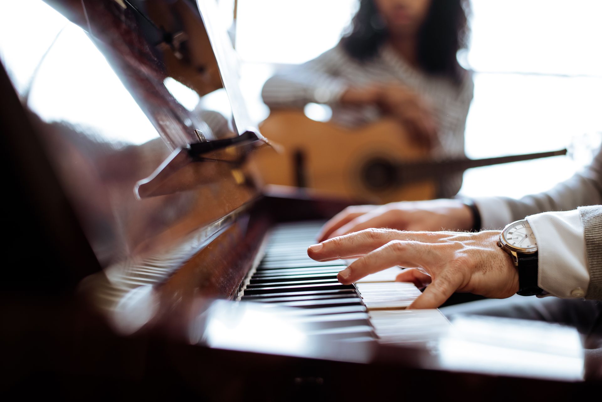 A man is playing a piano with a woman playing a guitar in the background.