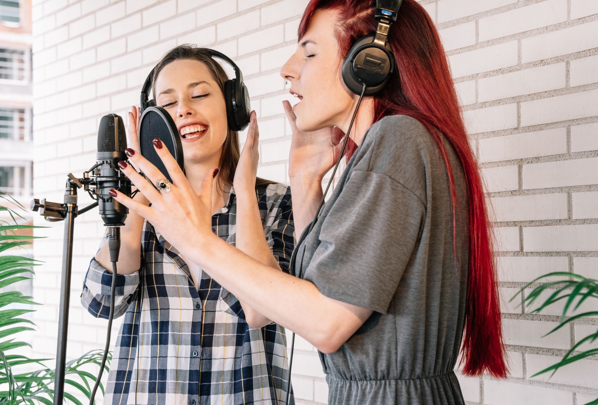 Two women are singing into a microphone while wearing headphones.