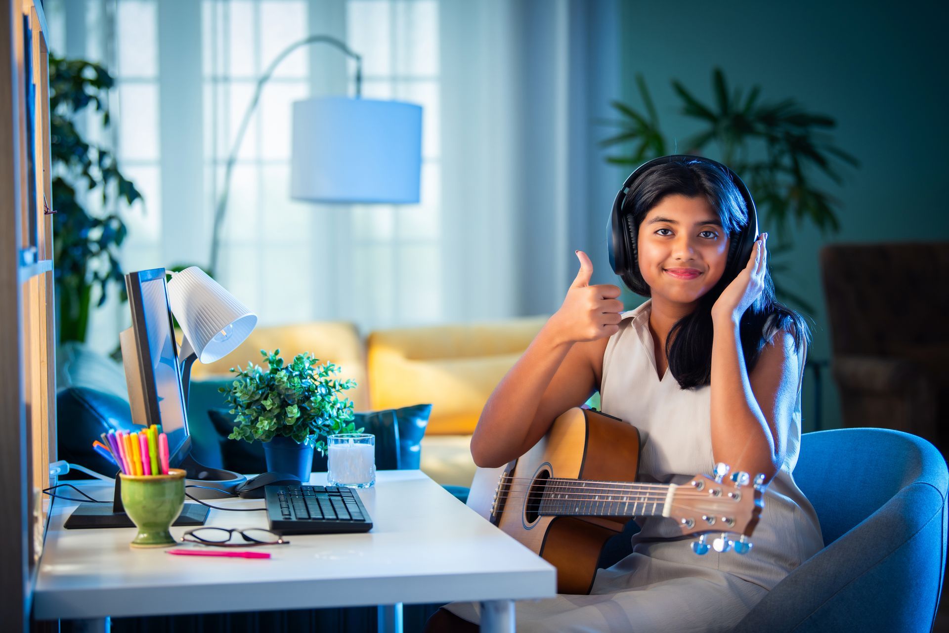 A young girl is sitting at a desk with a guitar and headphones on.