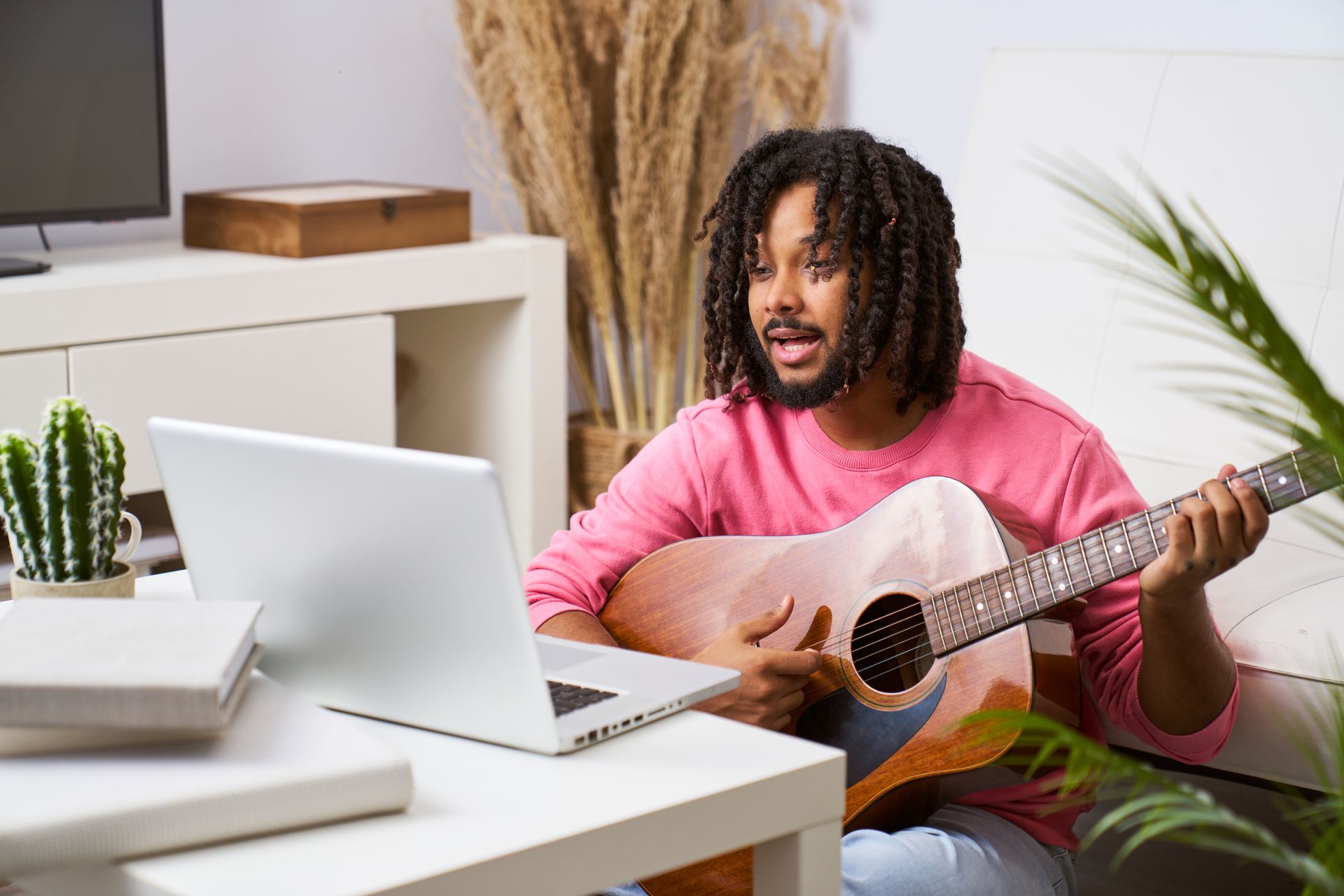 A man is playing a guitar in front of a laptop computer.