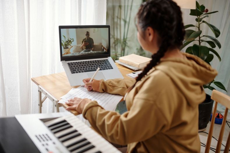 A woman is sitting at a desk with a laptop and a piano.