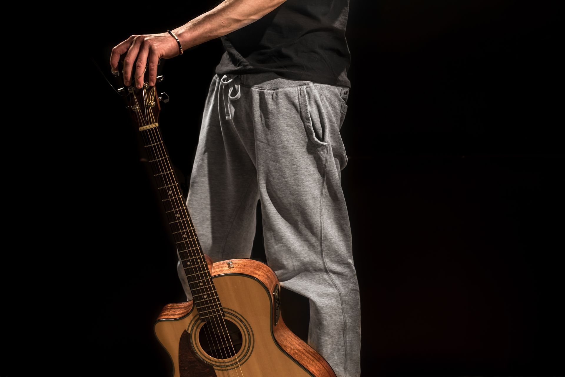 A man is holding an acoustic guitar in front of a black background.