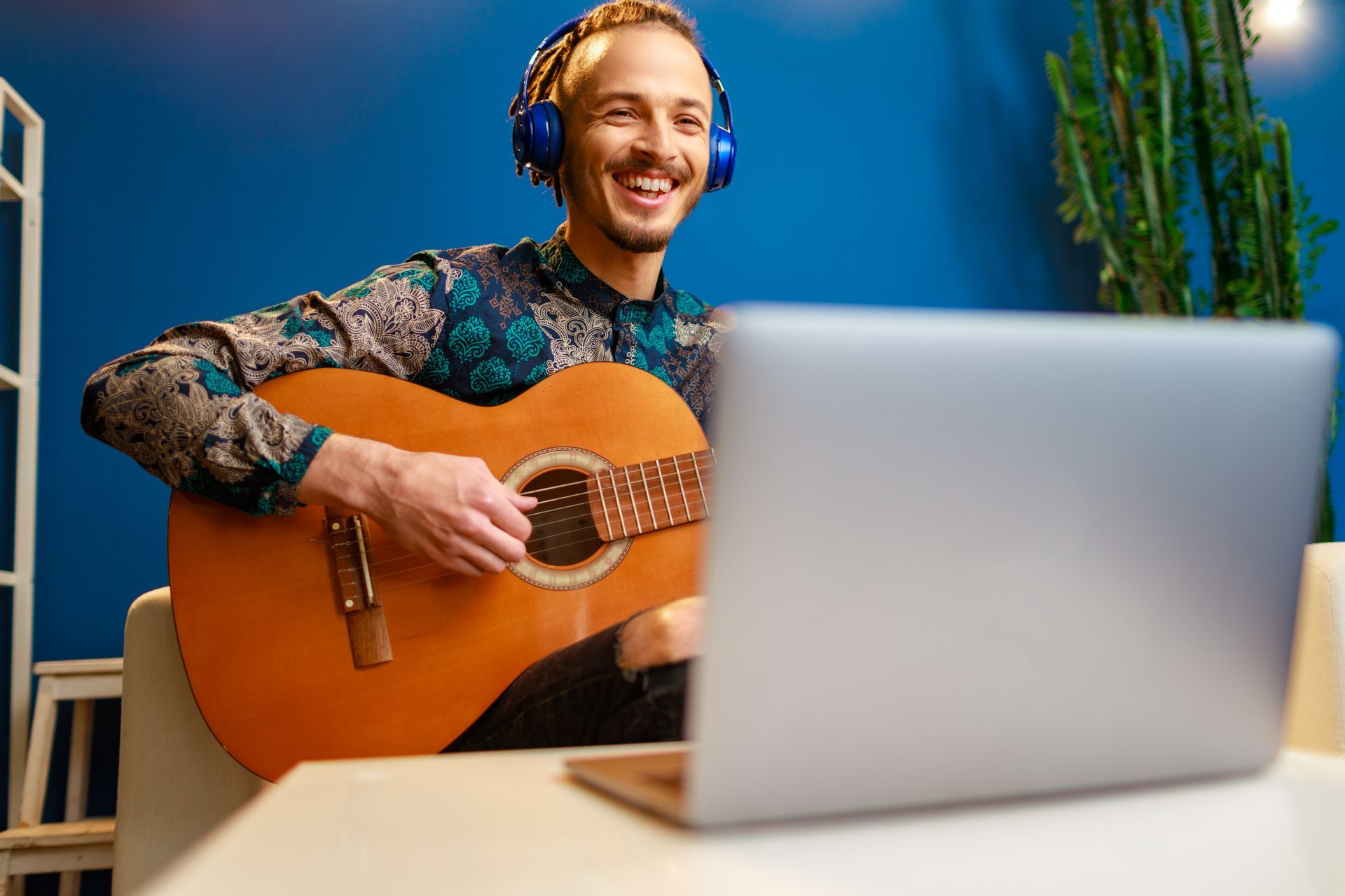 A man is playing an acoustic guitar in front of a laptop computer.