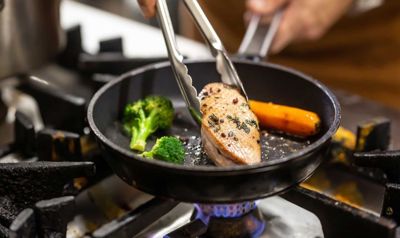 A person is cooking food in a frying pan on a stove.