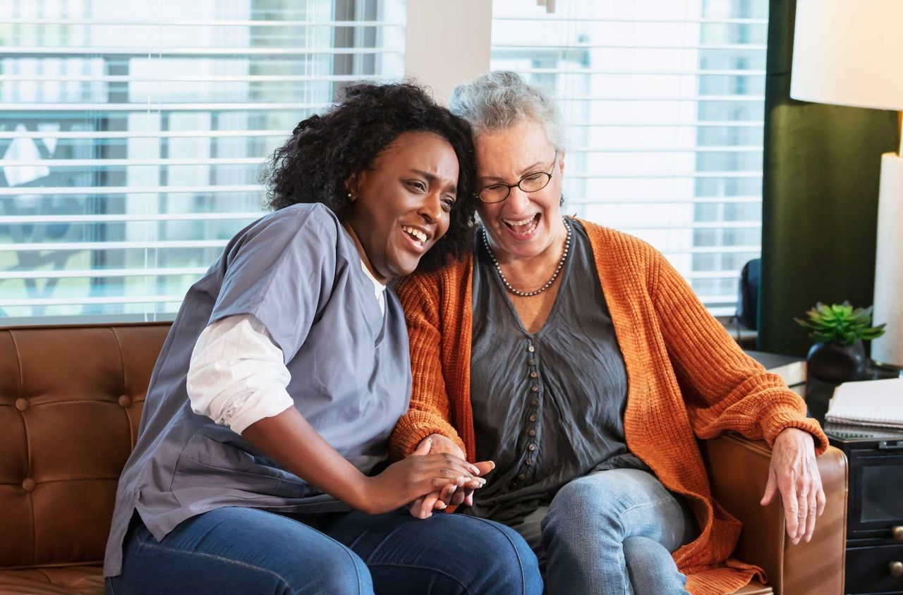 A nurse is sitting on a couch with an older woman.