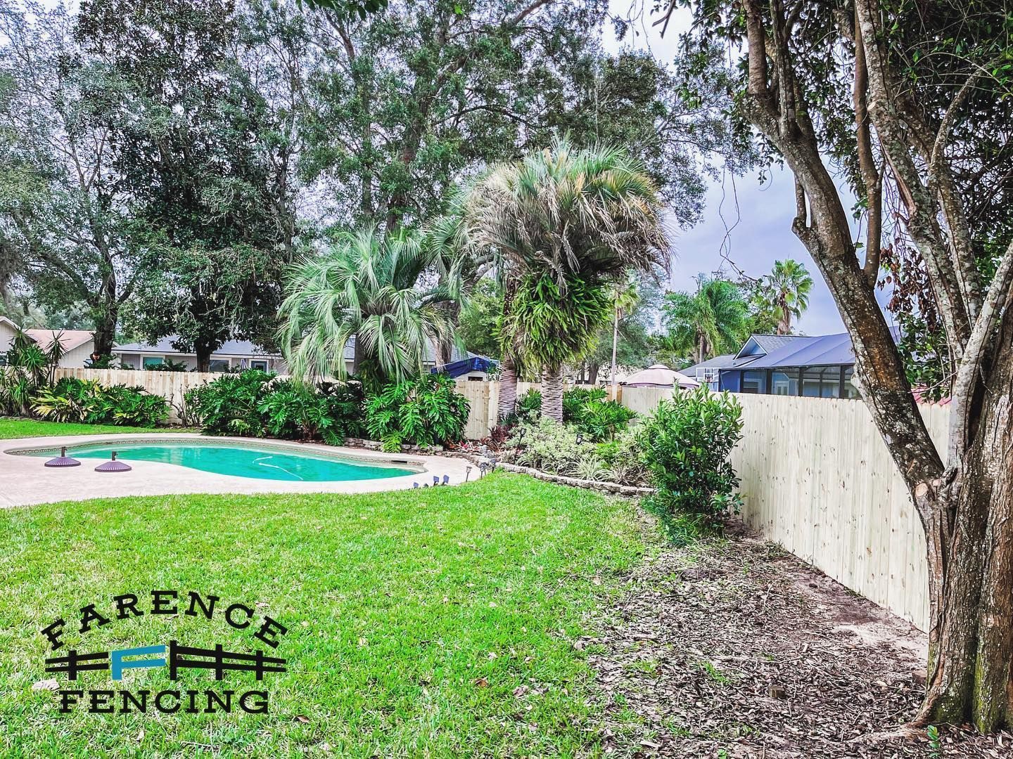 A backyard with a fence and a pool in the background.