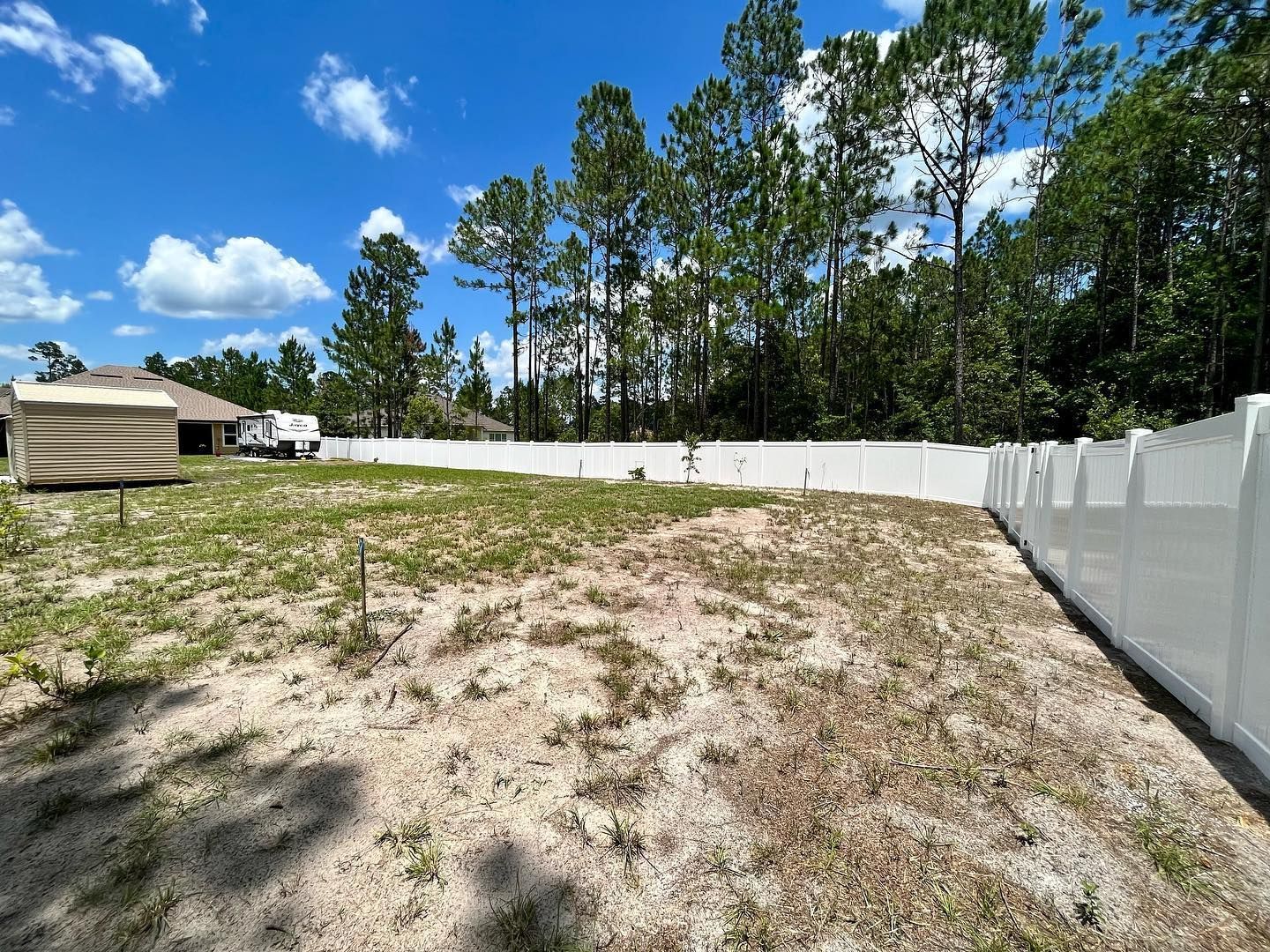 A white fence surrounds a dirt field with trees in the background.