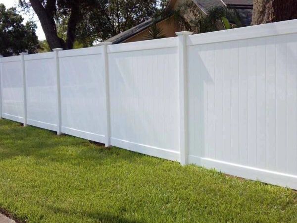 A white fence surrounds a lush green lawn in front of a house.