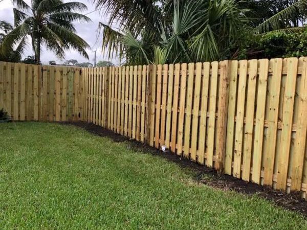 A wooden fence surrounds a lush green lawn in a backyard.