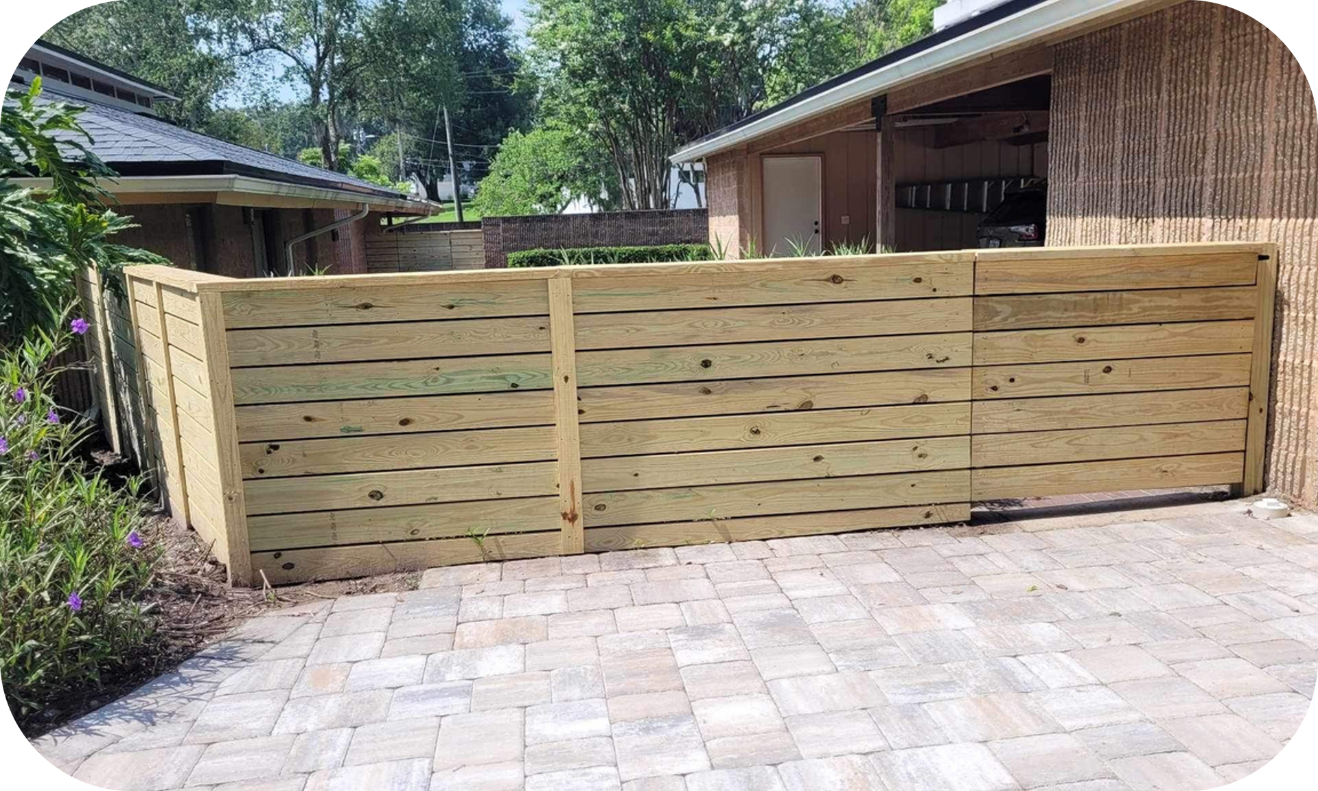 A wooden fence is sitting in front of a house on a brick driveway.