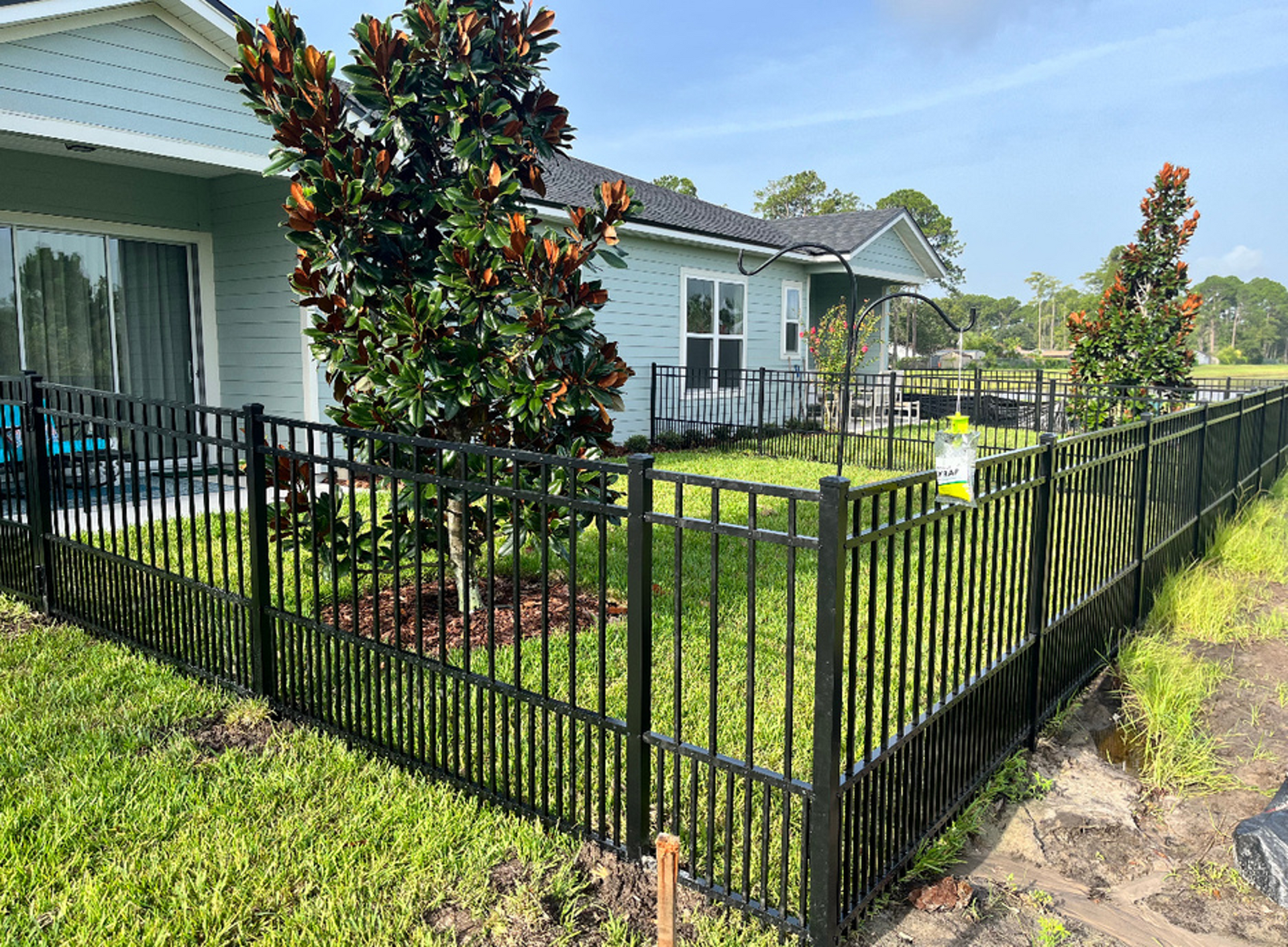 A black fence surrounds a lush green yard in front of a house.