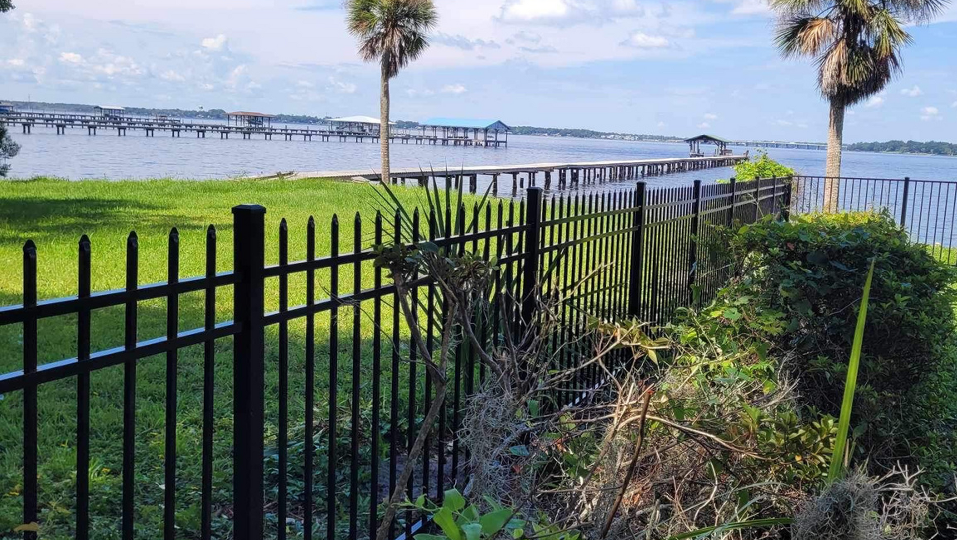 A black fence surrounds a grassy area next to a body of water.