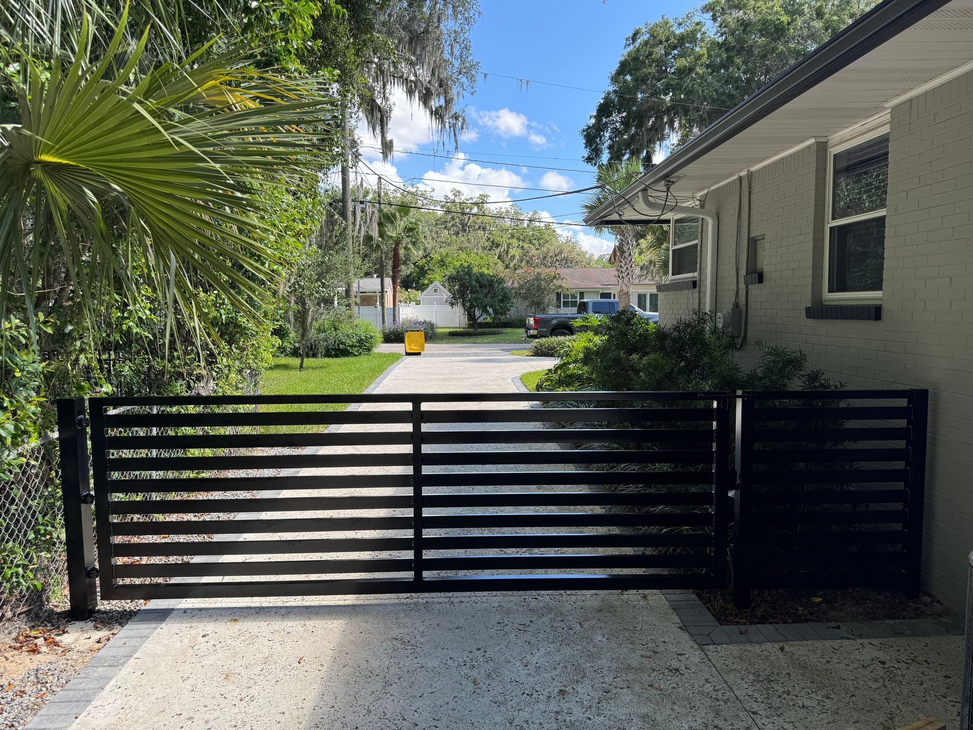 A black sliding gate is open to a driveway leading to a house.