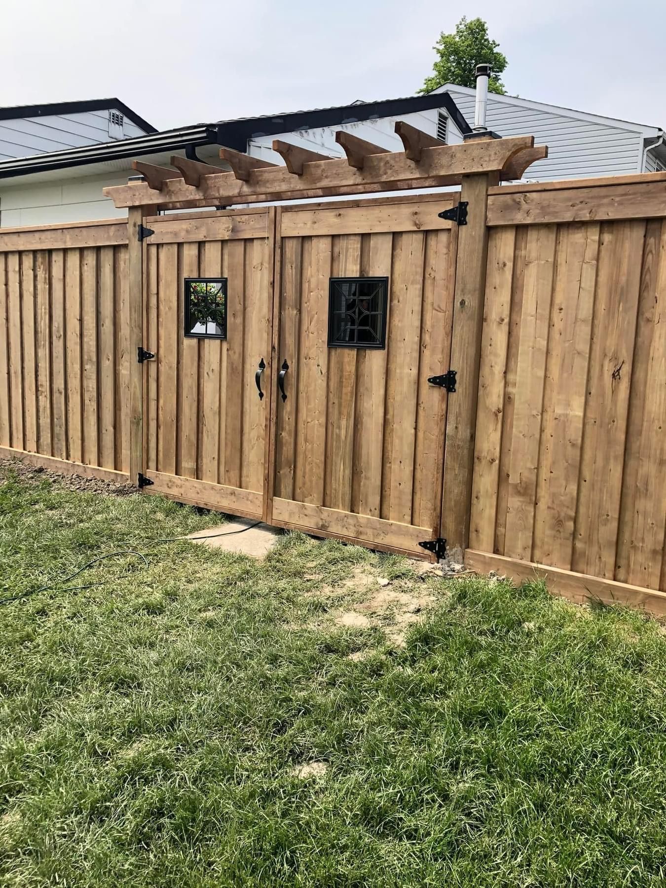 A wooden fence with a gate and pergola in the backyard of a house.