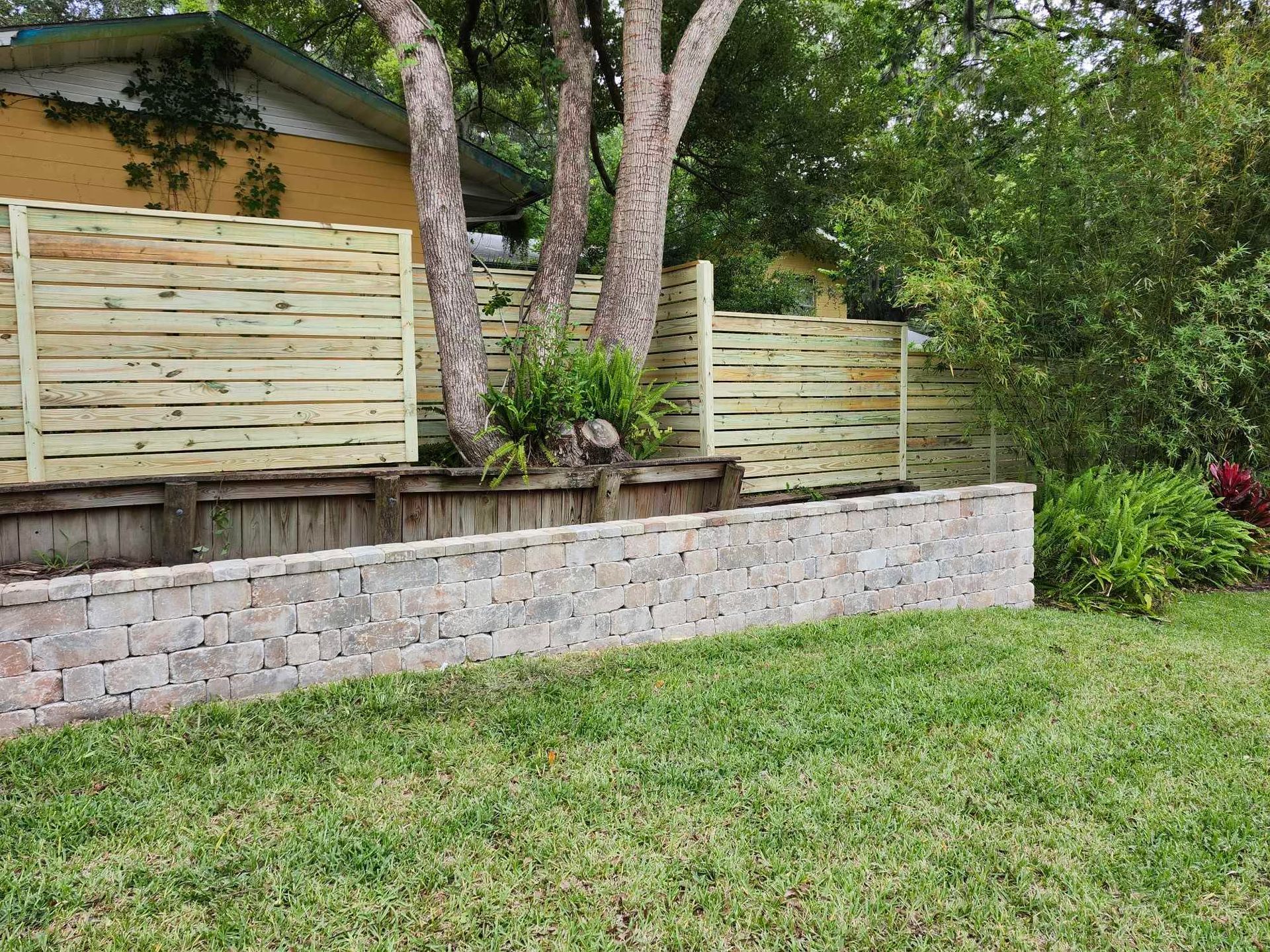 A wooden fence is surrounded by a stone wall in a backyard.