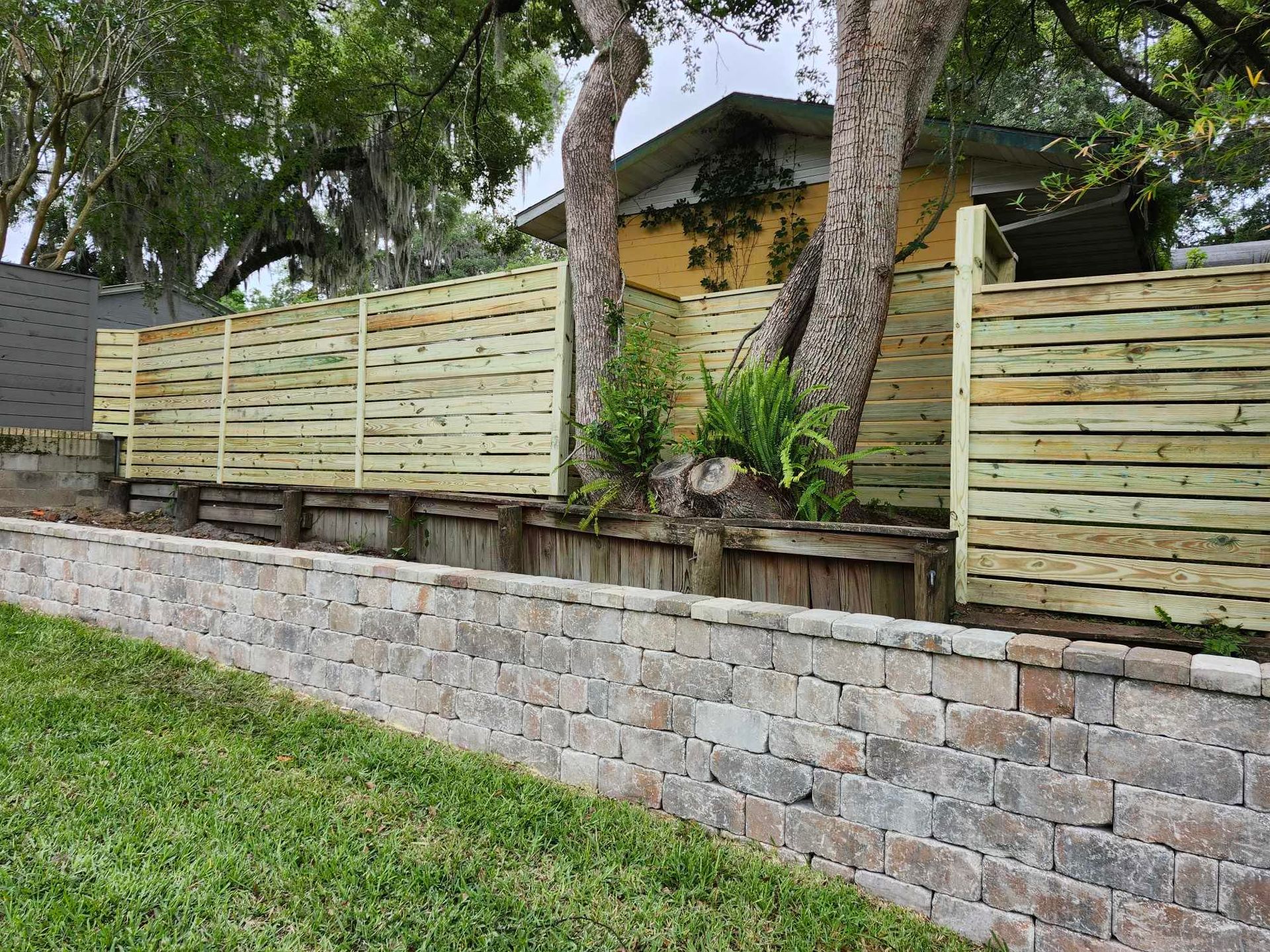 A wooden fence surrounds a brick wall in front of a house.