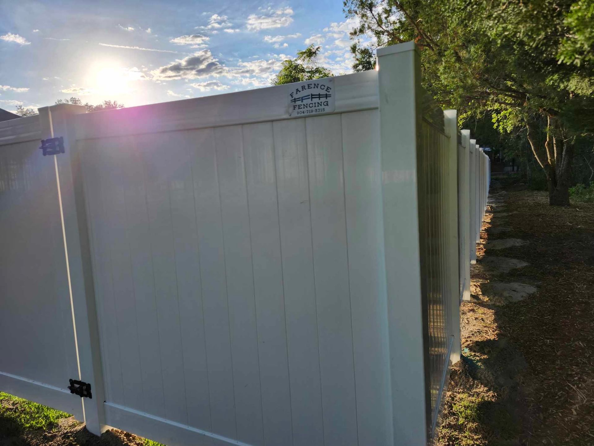 A white vinyl fence is surrounded by trees and a path.