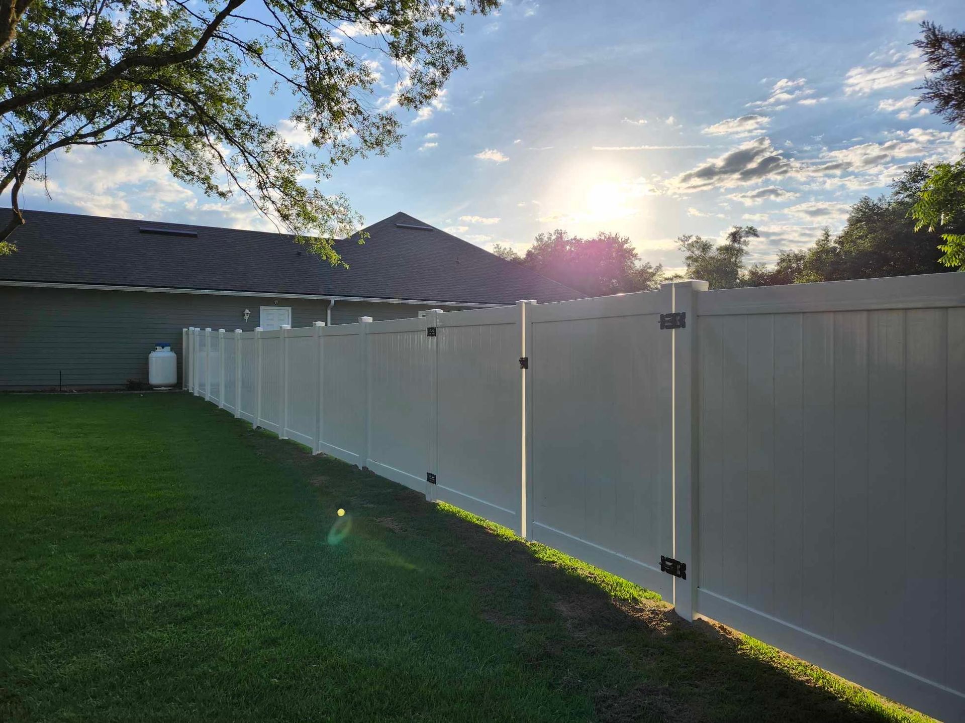 A white fence surrounds a lush green yard in front of a house.