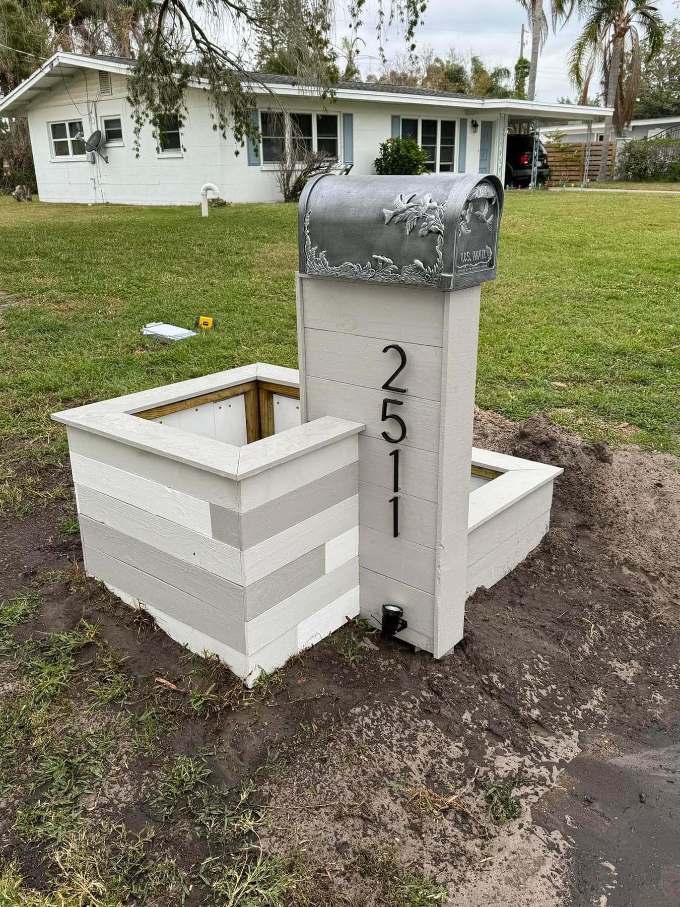 A mailbox is sitting in the middle of a grassy field in front of a house.
