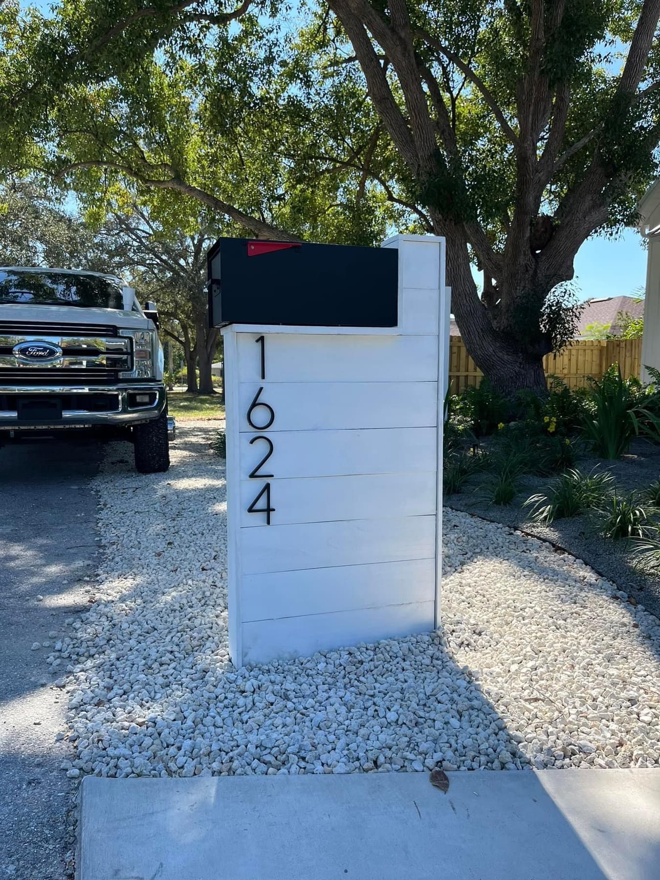 A white mailbox is sitting on the side of the road next to a truck.