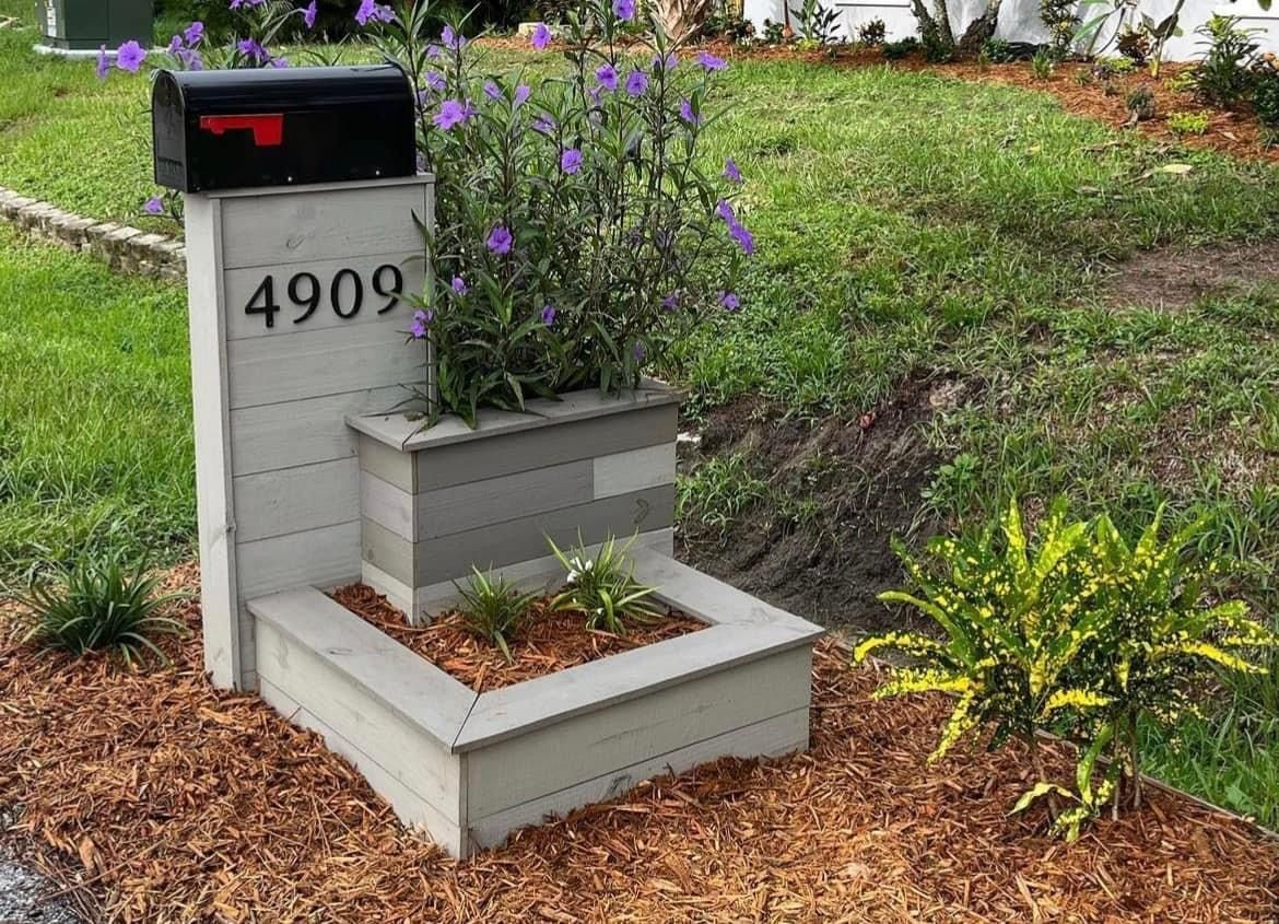 A mailbox is sitting next to a planter with purple flowers.