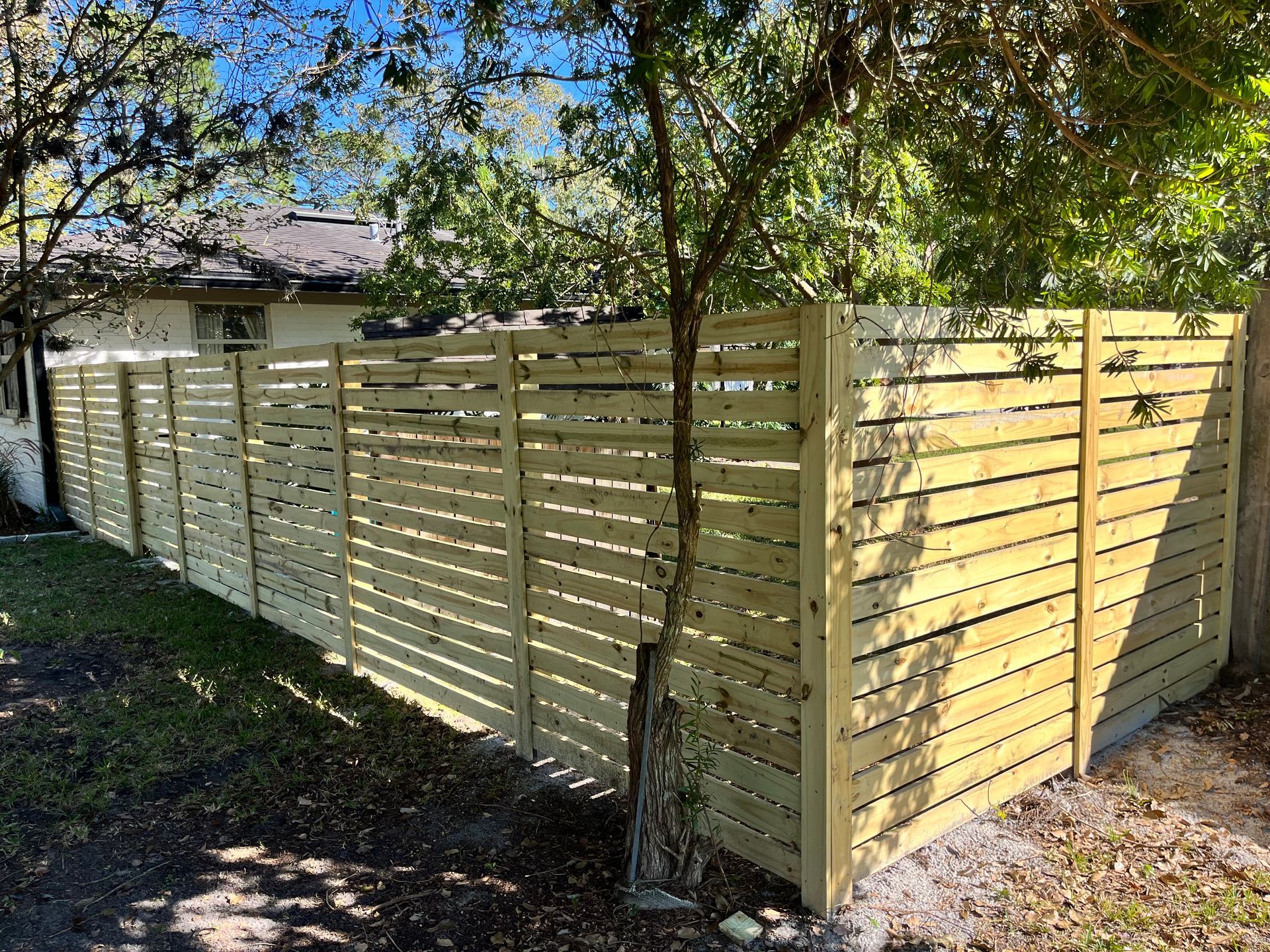 A wooden fence is surrounded by trees in front of a house.