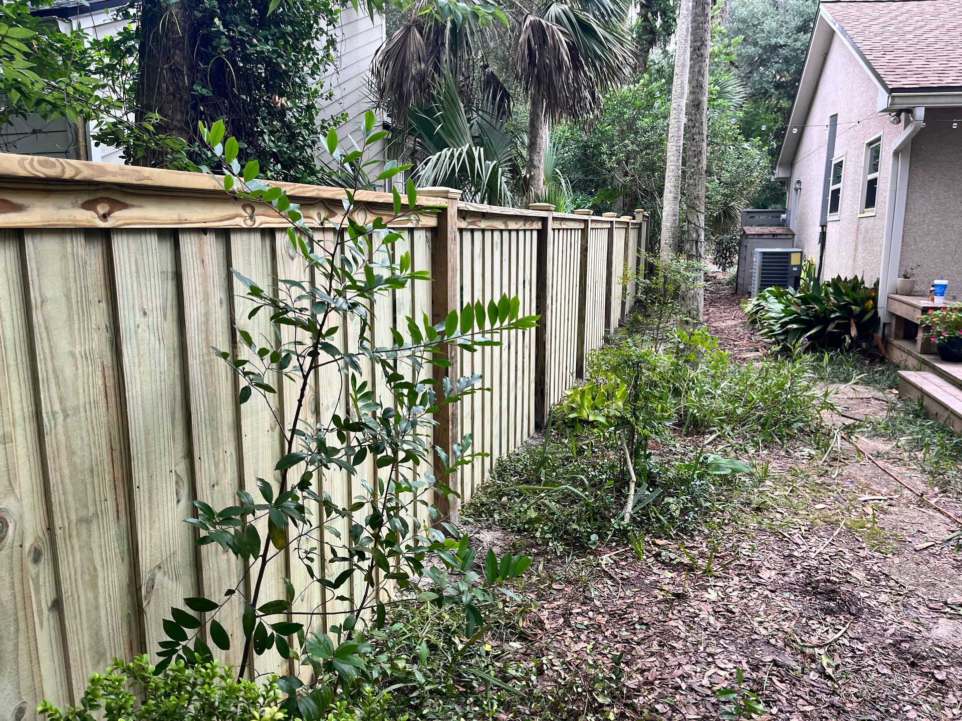 A wooden fence is surrounded by trees and bushes in the backyard of a house.